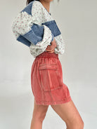 Person wearing a floral top and red cargo shorts on a plain background