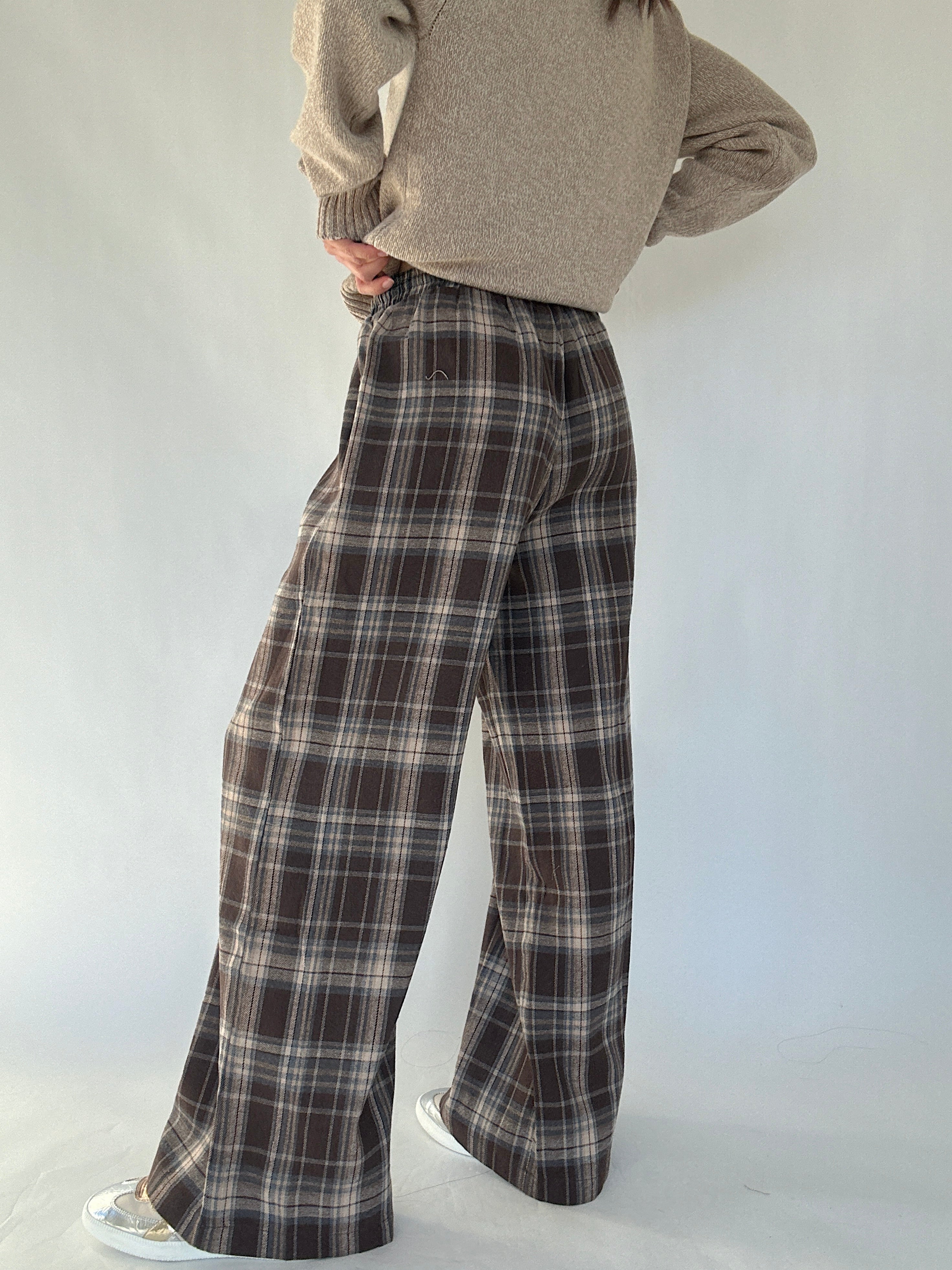 Person wearing plaid pants and a beige sweater on a white background from the back