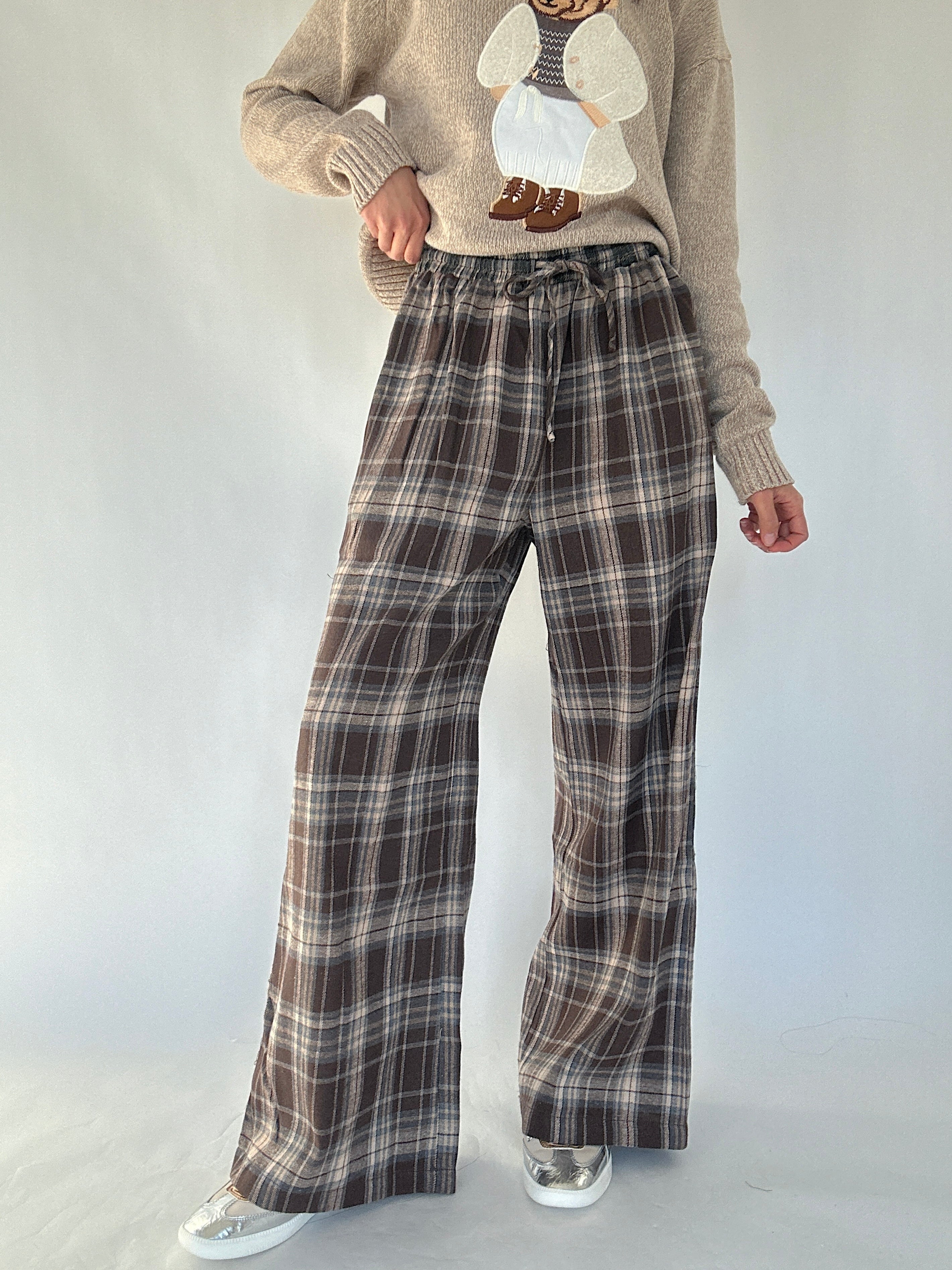 Person wearing brown plaid wide leg pants and a beige sweater on a white background