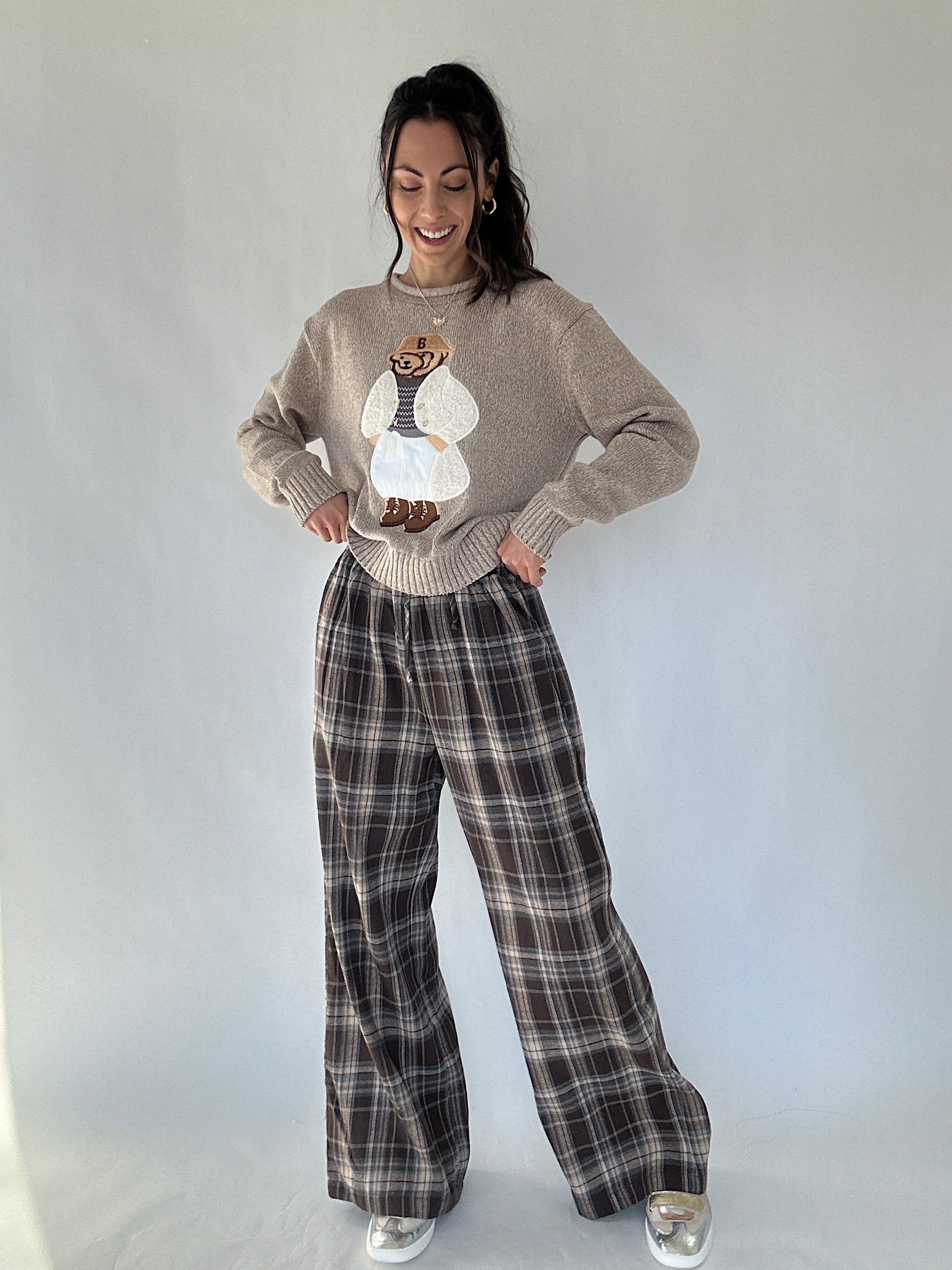 Woman wearing a graphic sweater and brown plaid wide leg pants against a plain background
