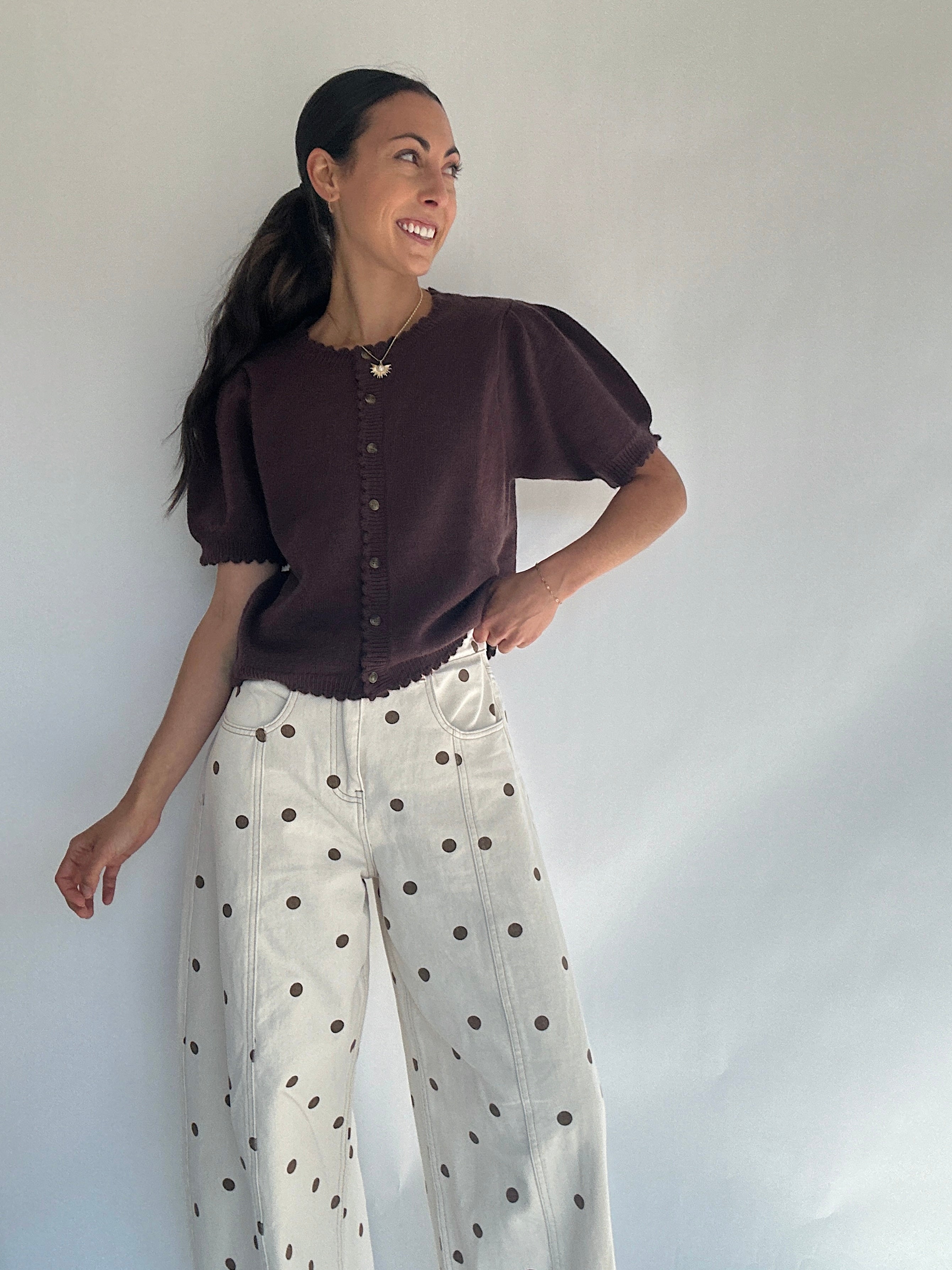 Woman wearing a brown short sleeve knit top and polka dot pants against a white background