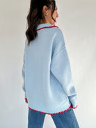 Light blue sweater with red trim worn by a person against a white background back view