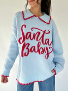Light blue sweater with red 'Santa Baby' text worn by a person on a white background