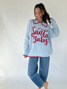 Woman wearing a light blue sweater with 'Santa Baby' text and red trim on a white background