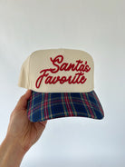 Cap with 'Santa's Favorite' text and plaid bill held by a hand against a white background