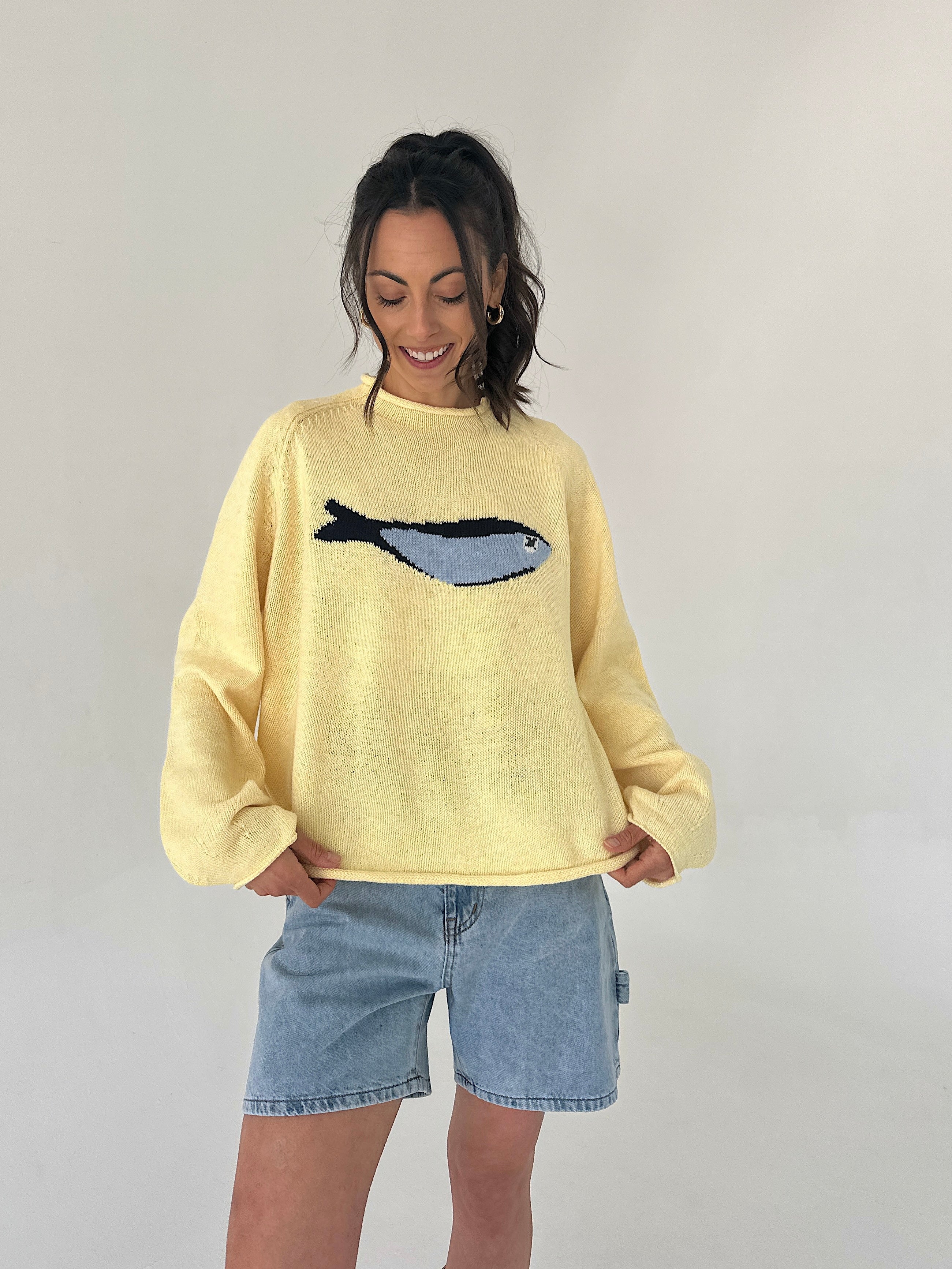 Person wearing a yellow sweater with a fish design on a plain background