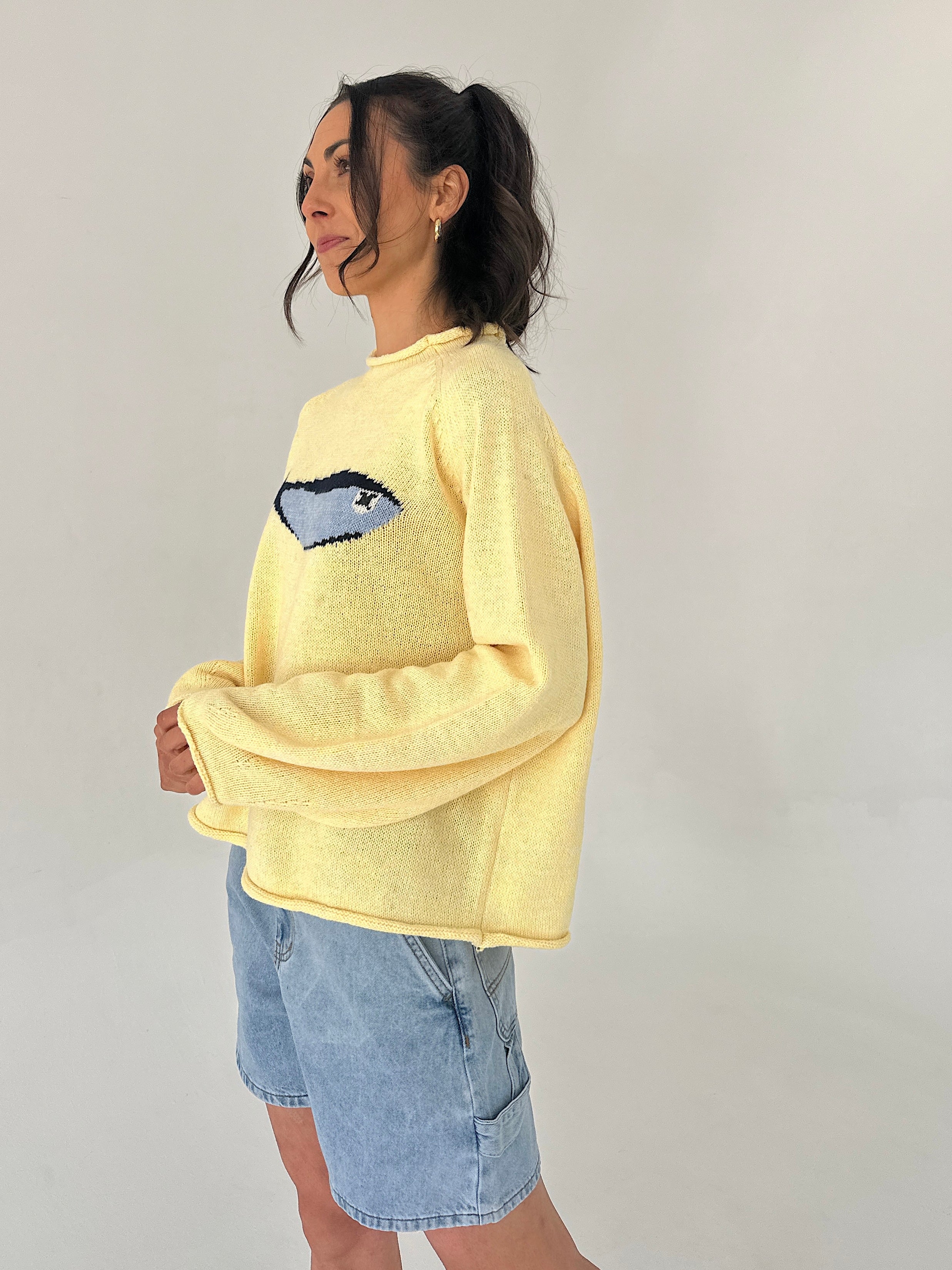 Person wearing a yellow sweater with a blue fish graphic on a plain background