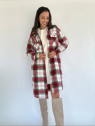A woman wearing a red and green plaid jacket with a longline silhouette, button front, and side pockets paired with a white top and beige boots.