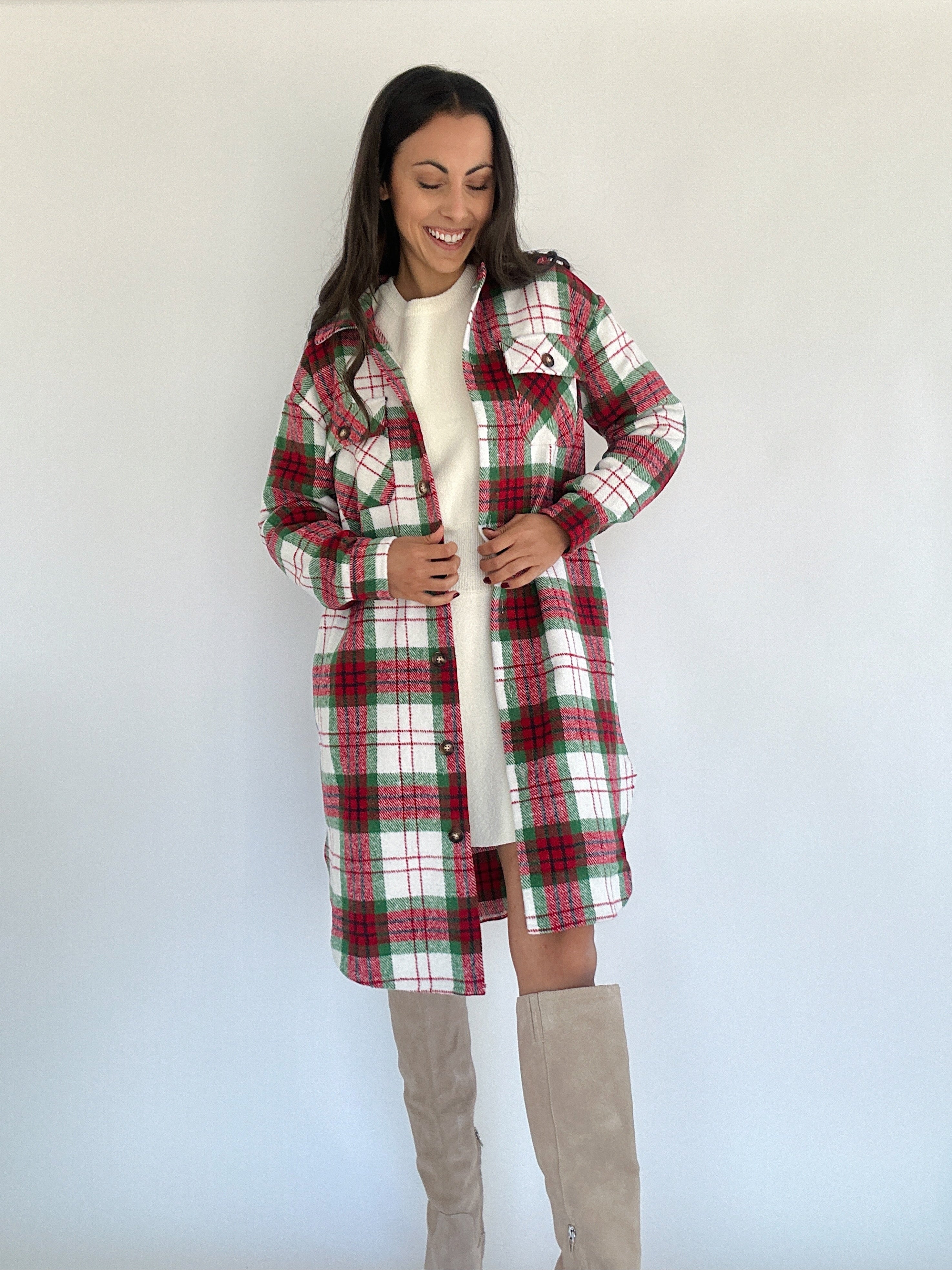 A woman wearing a red and green plaid jacket with a longline silhouette, button front, and side pockets paired with a white top and beige boots.
