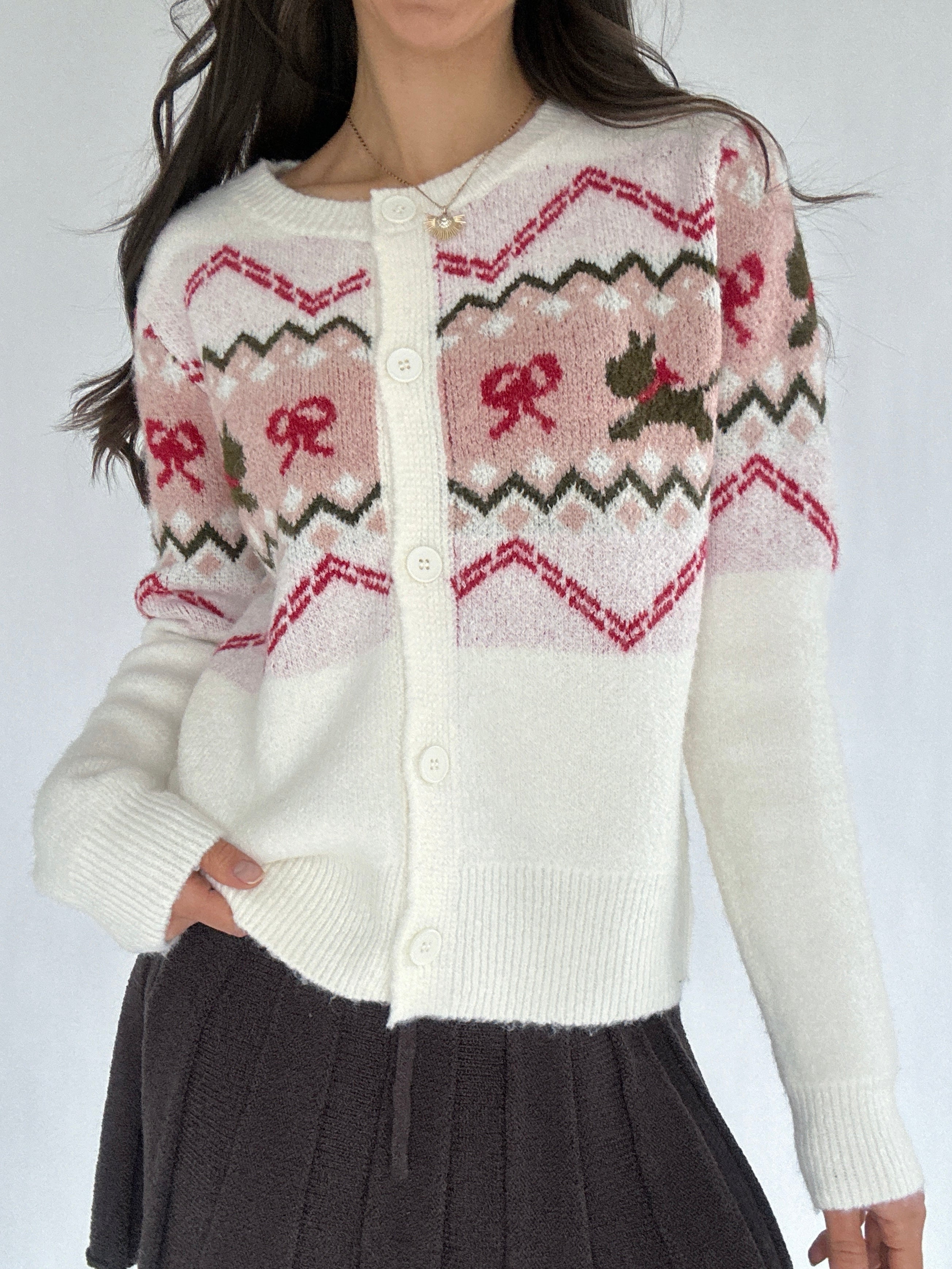 Person wearing a white cardigan with pink and red pattern on a plain background