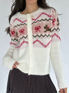 Person wearing a white cardigan with pink and red pattern on a plain background