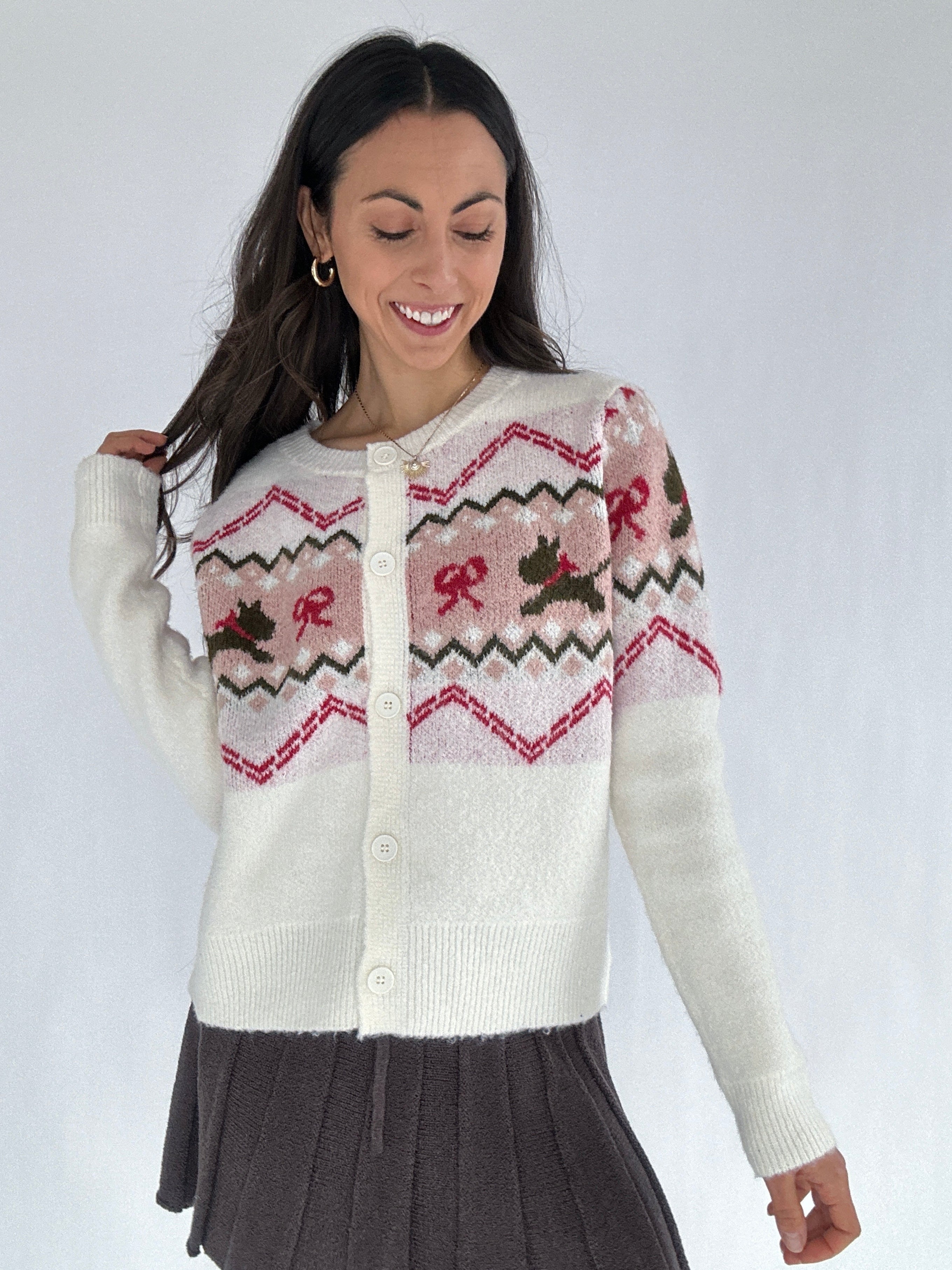 Woman wearing a white cardigan with pink and brown patterns on a plain background
