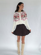 Woman wearing a scotty dog and bow patterned sweater, brown mini skirt, and beige knee-high boots on a white background