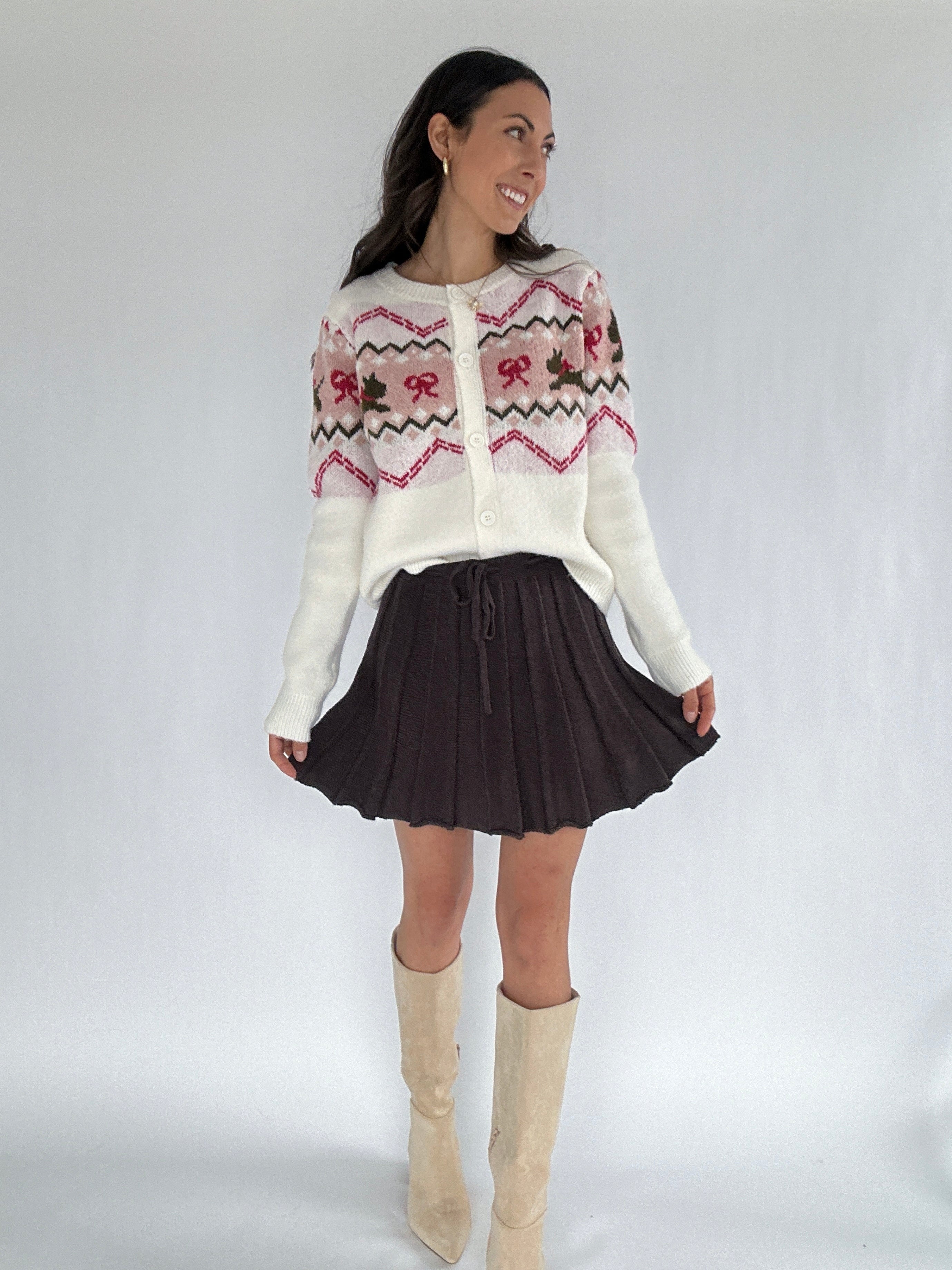 Woman wearing a scotty dog and bow patterned sweater, brown mini skirt, and beige knee-high boots on a white background