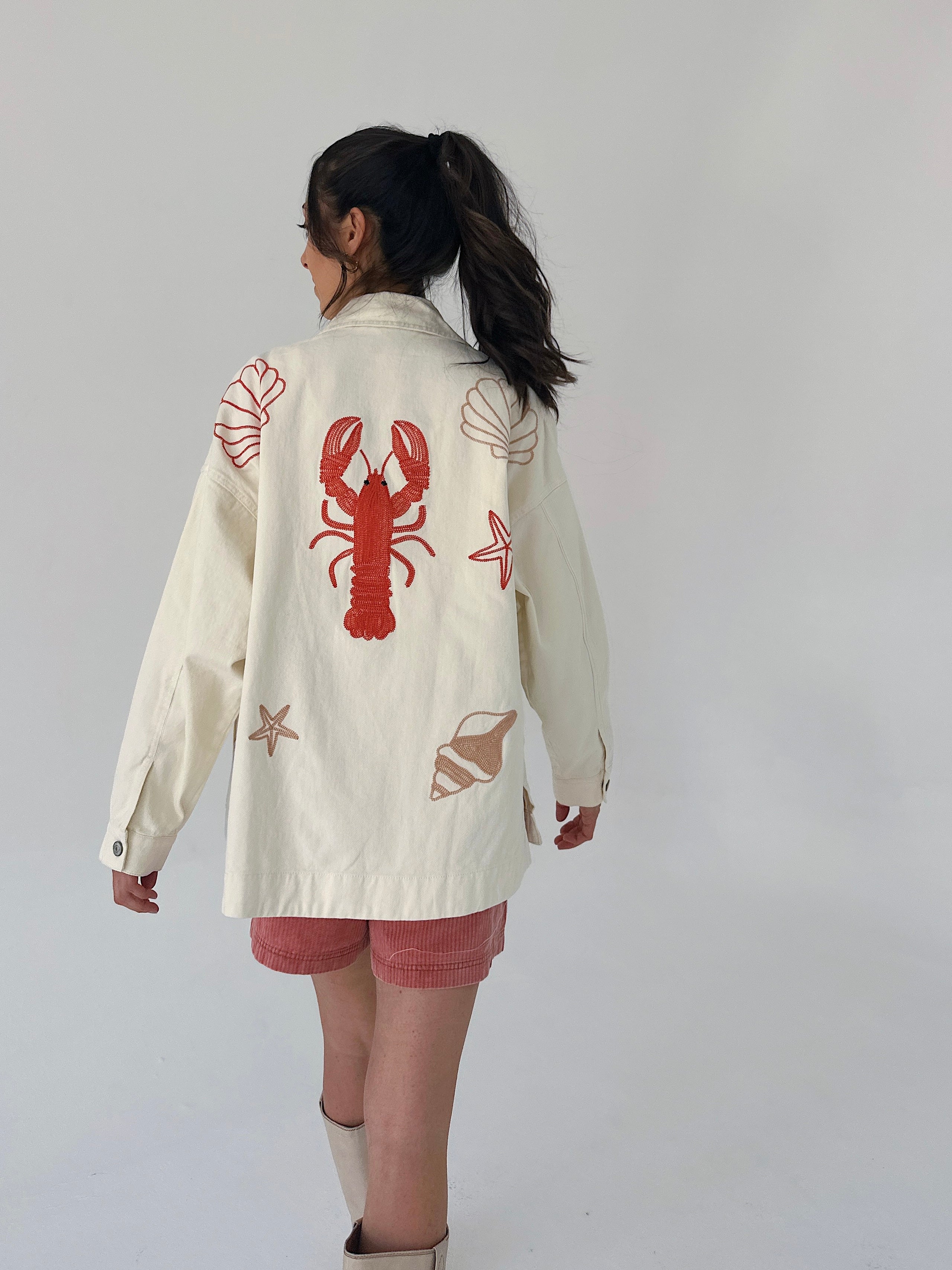 Person wearing a cream-colored jacket with red lobster design on a plain background
