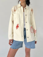 Person wearing a cream jacket with red shell designs on a plain background