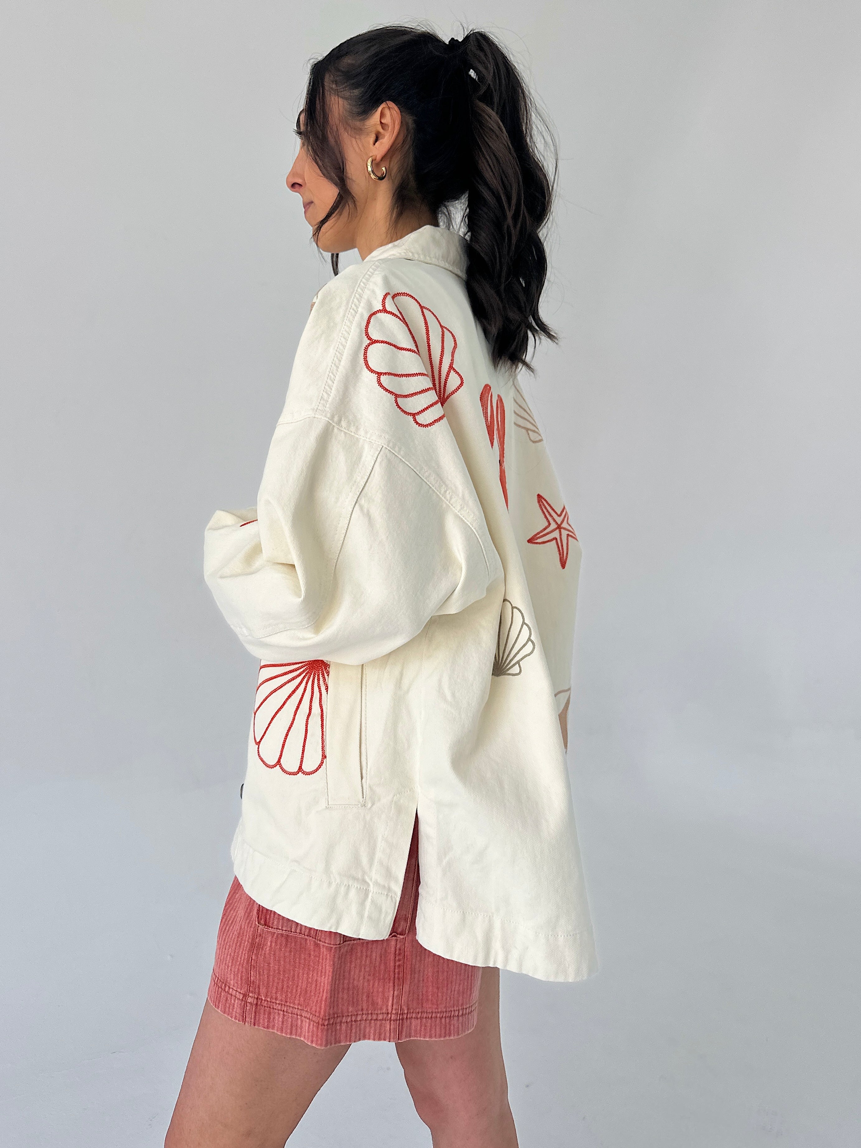 Person wearing a white jacket with red seashell patterns on the back, standing against a plain background