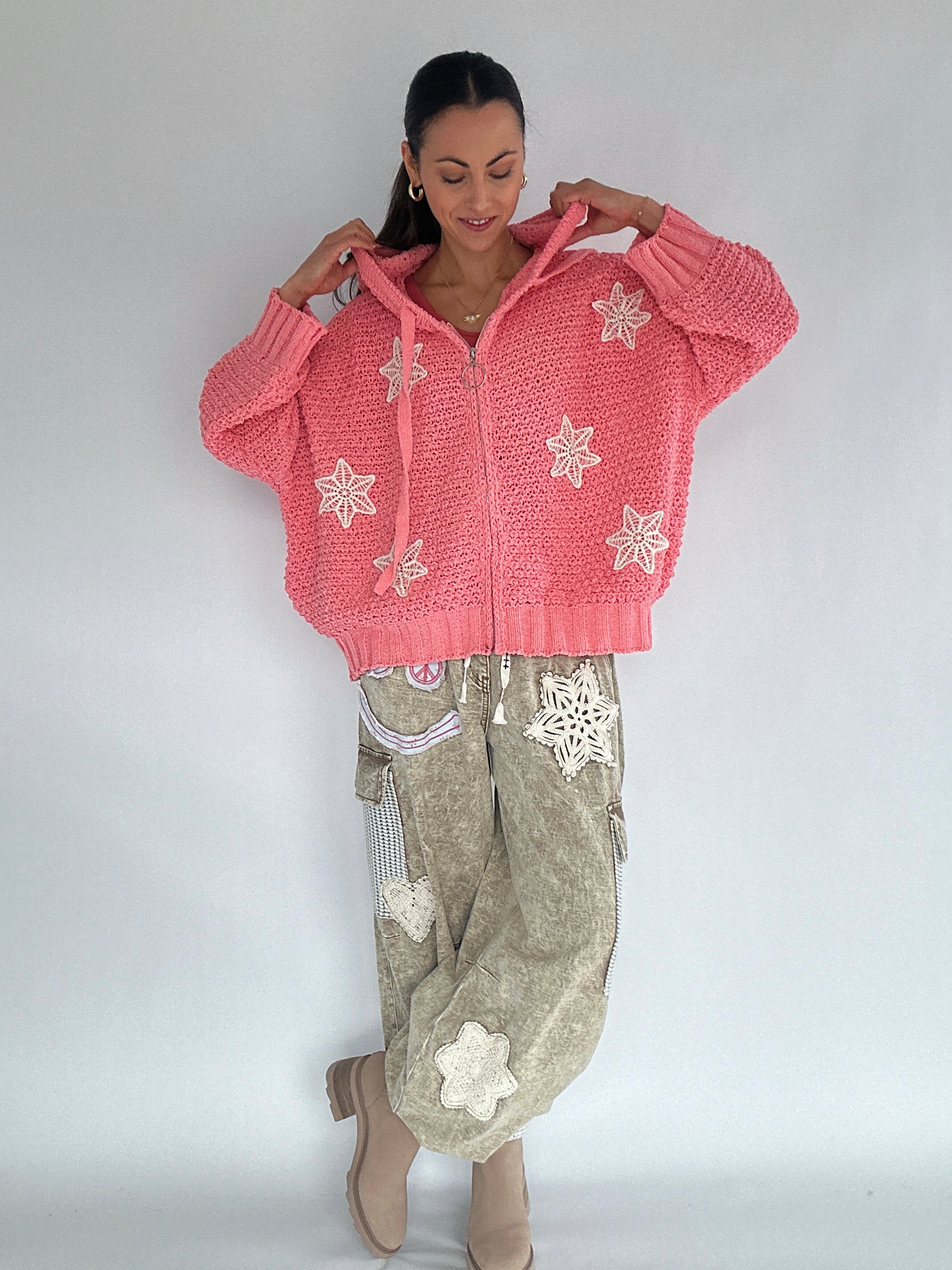 Woman wearing a pink knitted zip up hoodie with snowflake patterns on a plain background