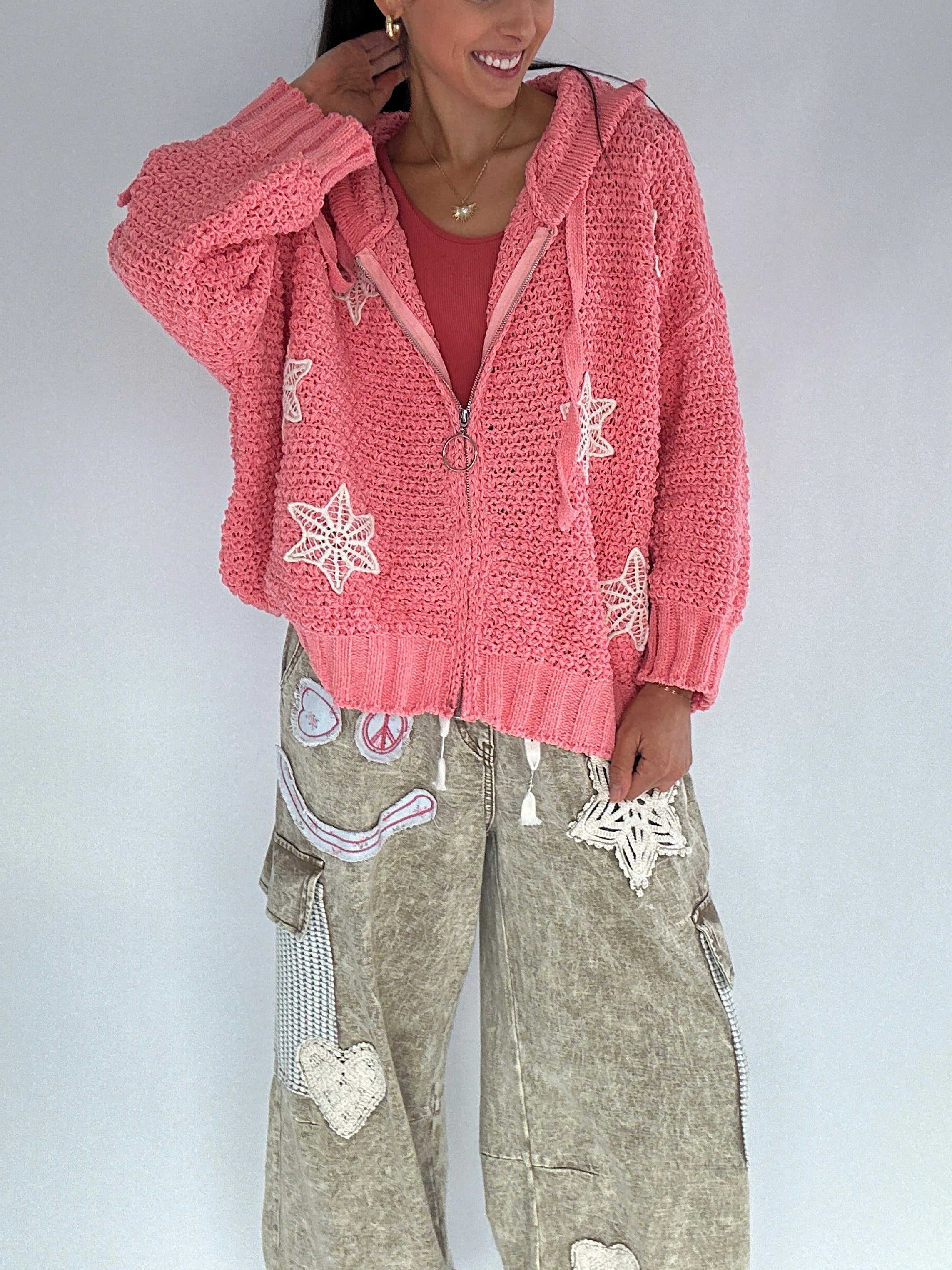 Person wearing a pink zip up chenille hooded cardigan with crochet snowflake patterns on a plain background