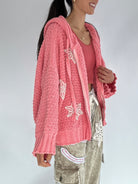 Person wearing a pink knitted cardigan with snowflake patterns on a plain background