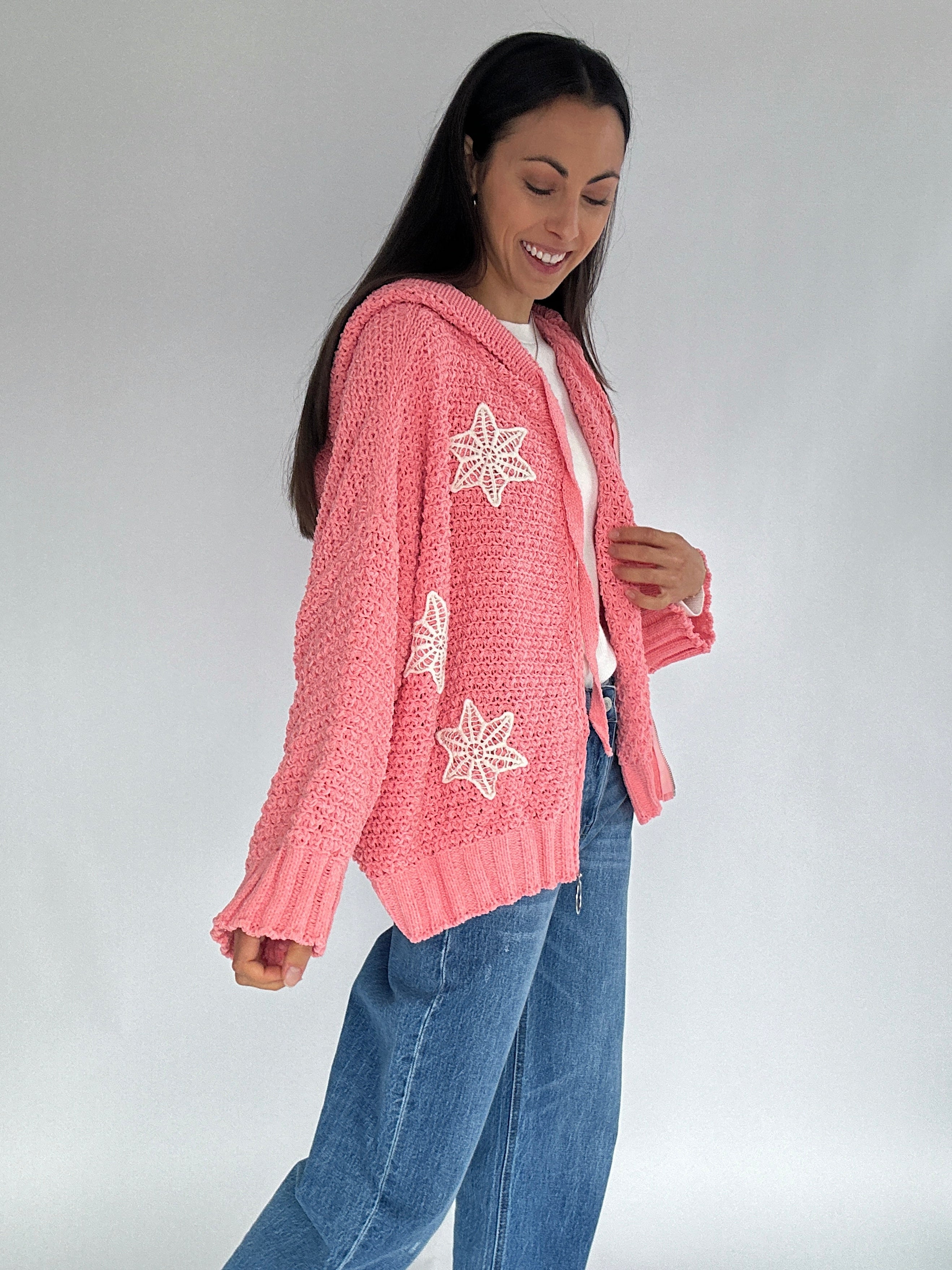 Woman wearing a pink cardigan with crochet patterns on a plain background from side