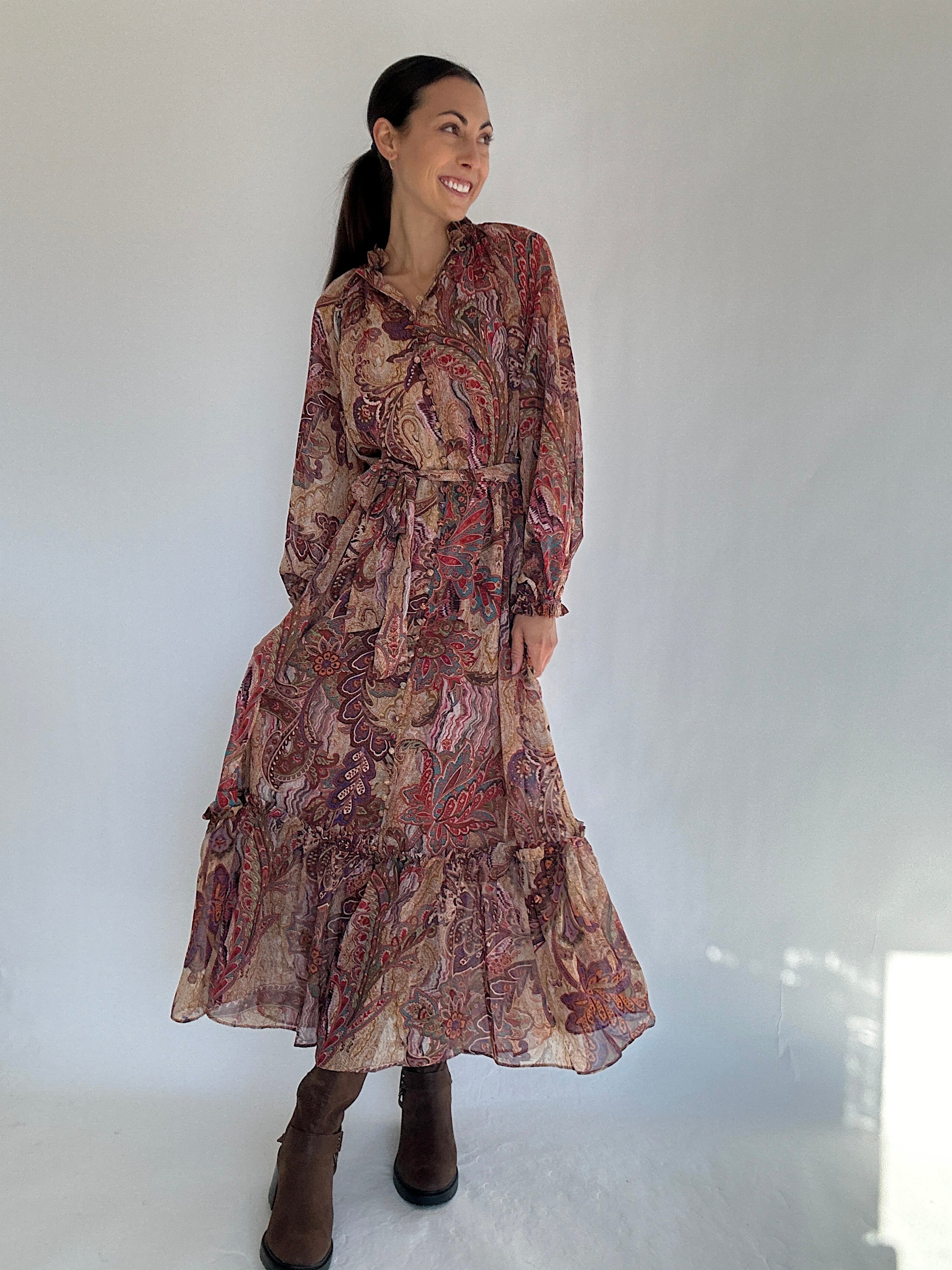 Woman wearing a boho paisley patterned maxi dress in warm tones against a white background