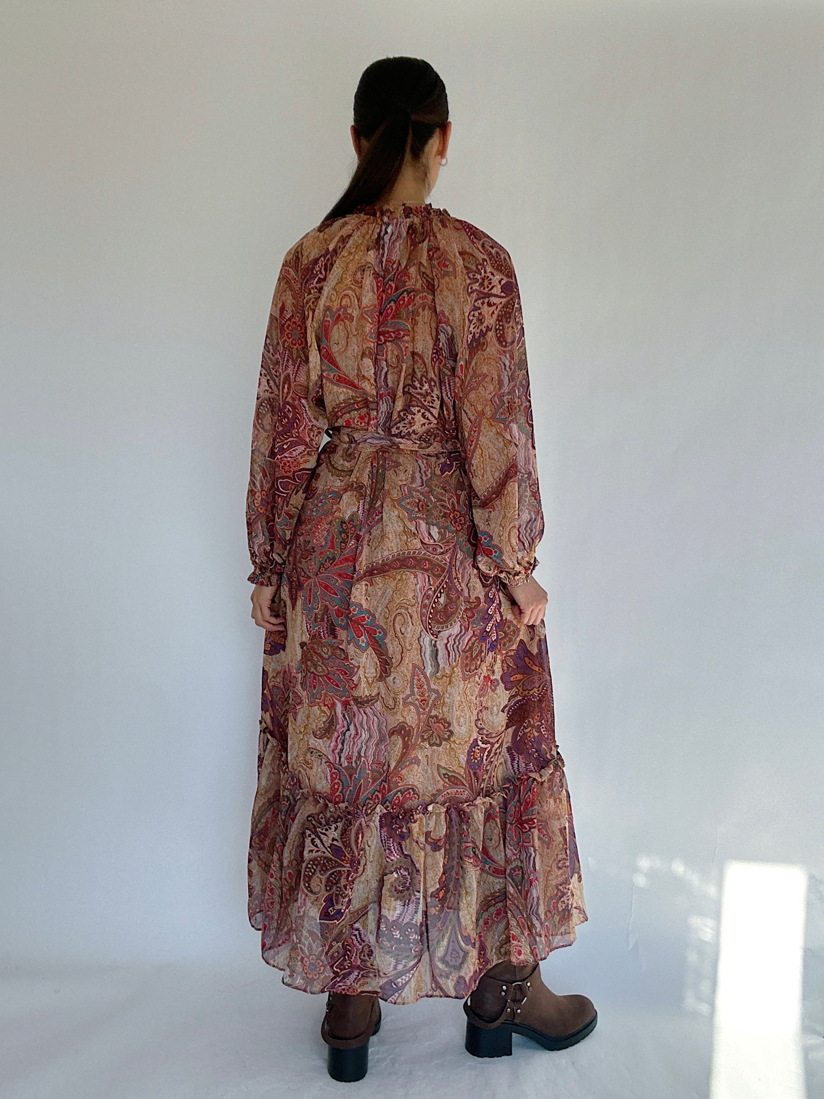 Woman wearing a long, boho paisley patterned dress against a white background showing off the back view