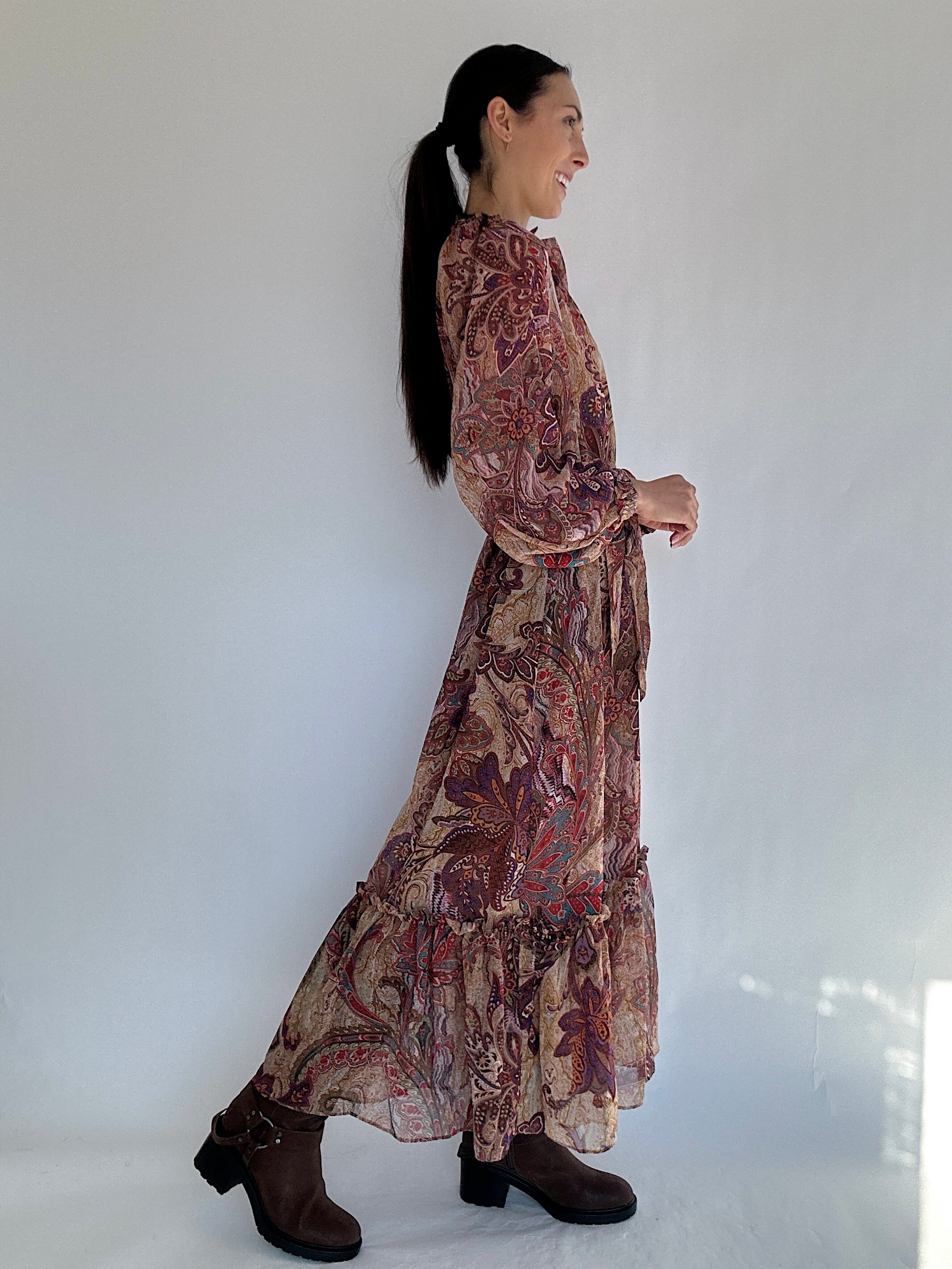 Woman wearing a long, boho paisley patterned dress against a white background showing the side view