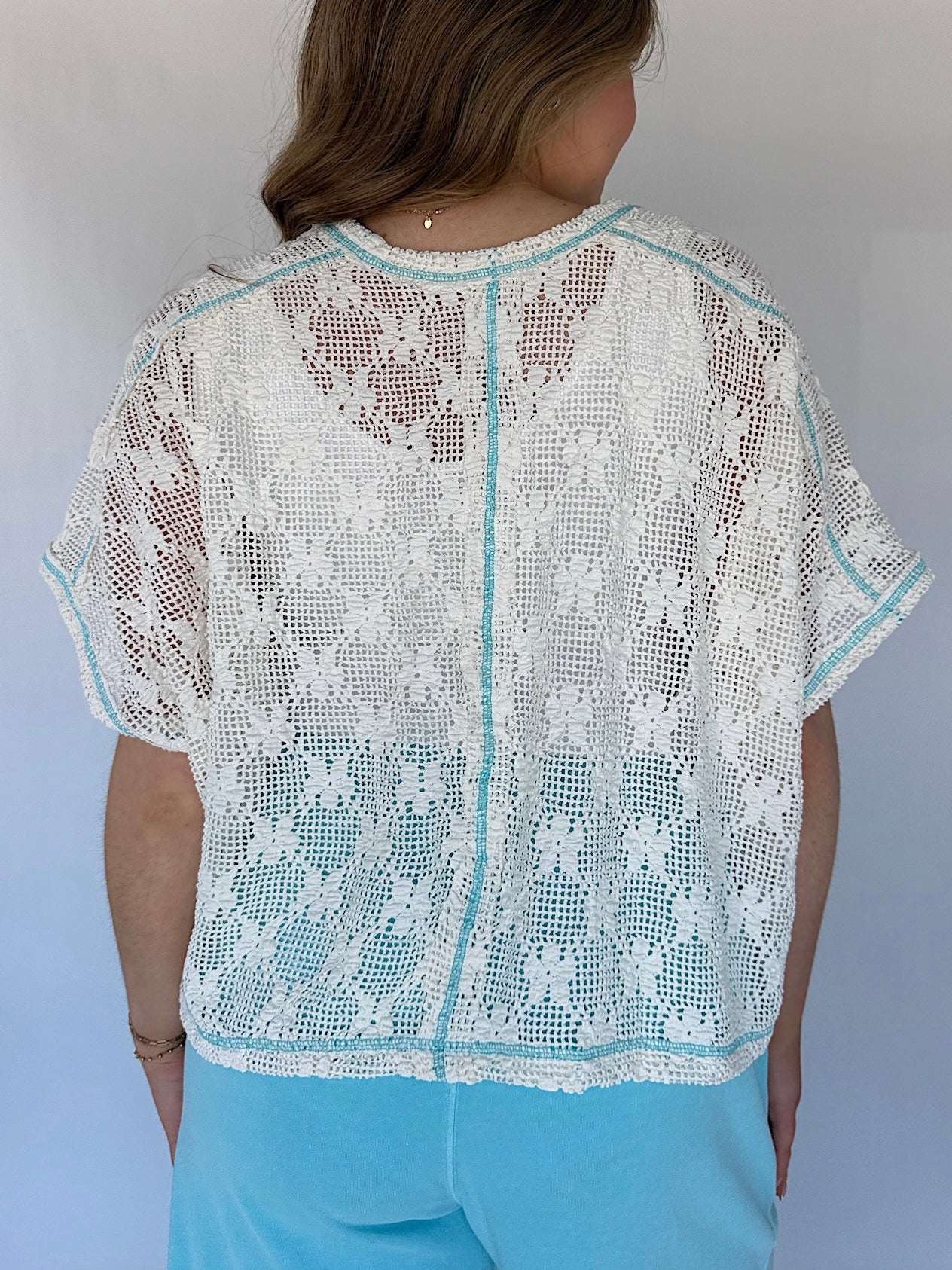 Person wearing a white lace top with short sleeves against a plain background