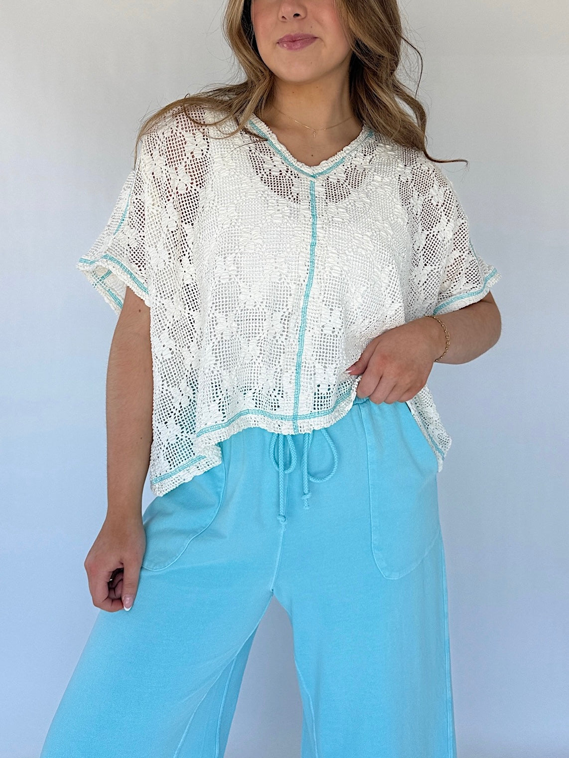 Woman wearing a white lace top and light blue pants against a plain background