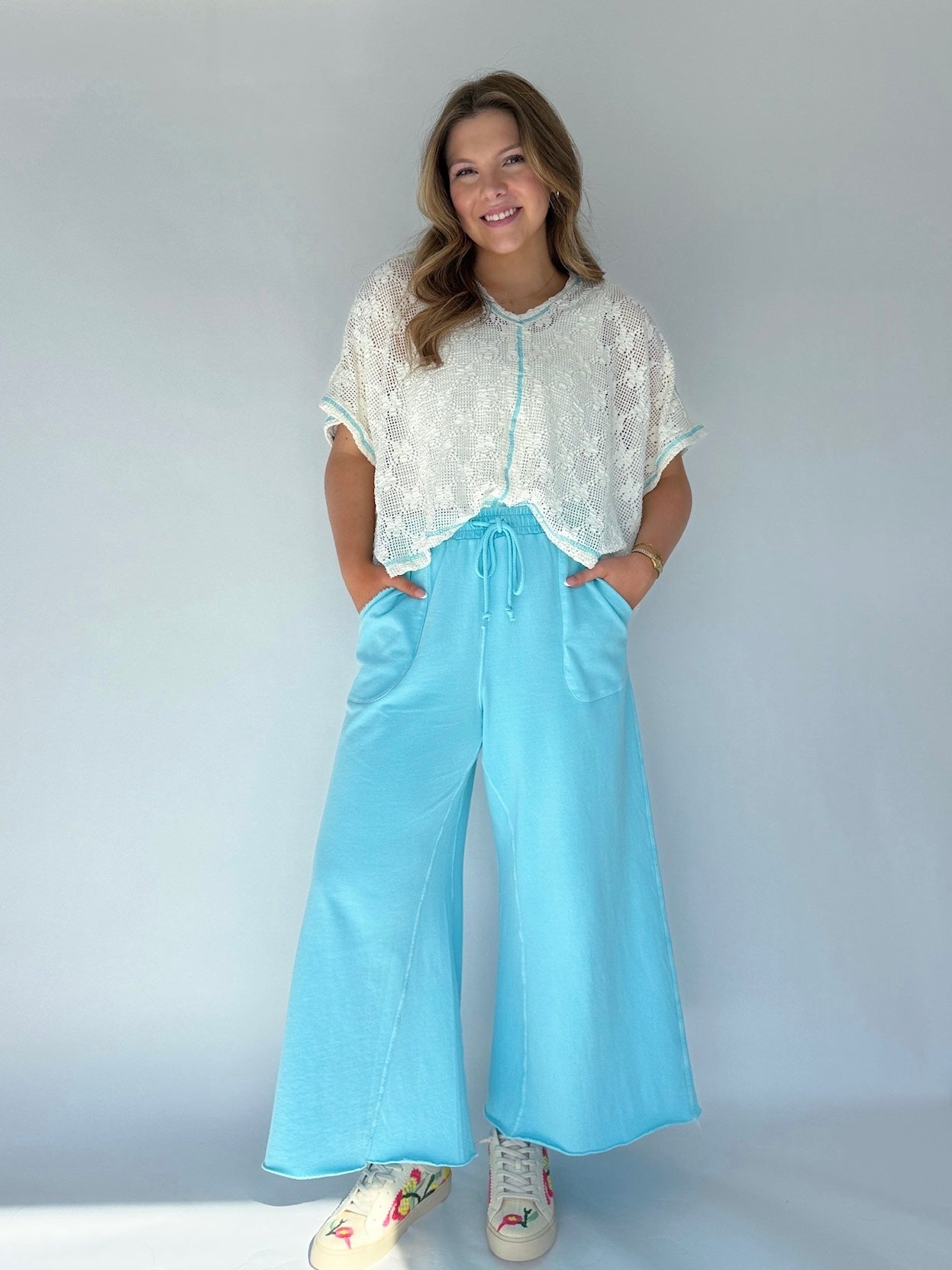 Person wearing a white lace top and light blue wide-leg pants on a plain background