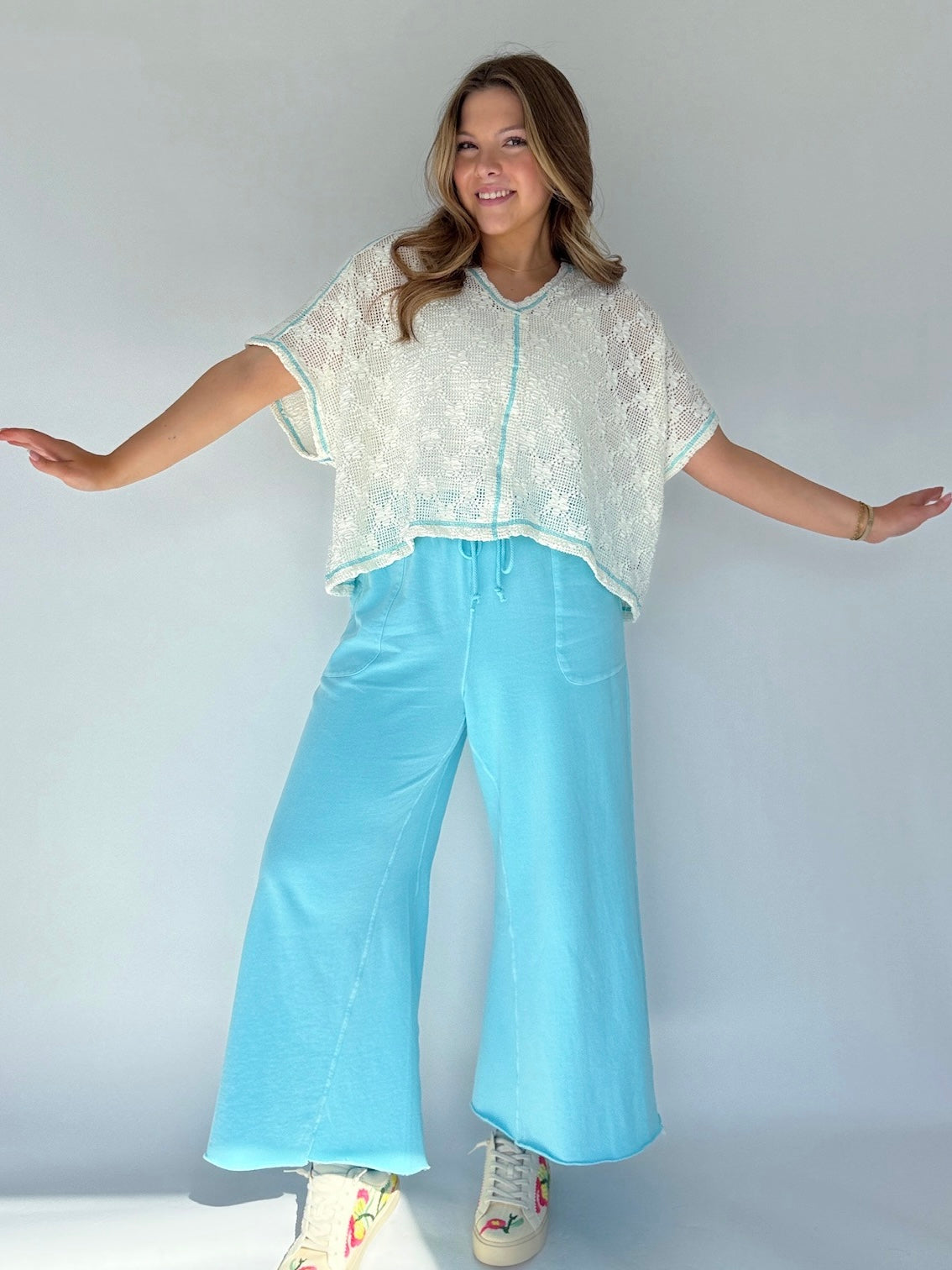 Woman wearing a light-colored top and light blue pants against a plain background