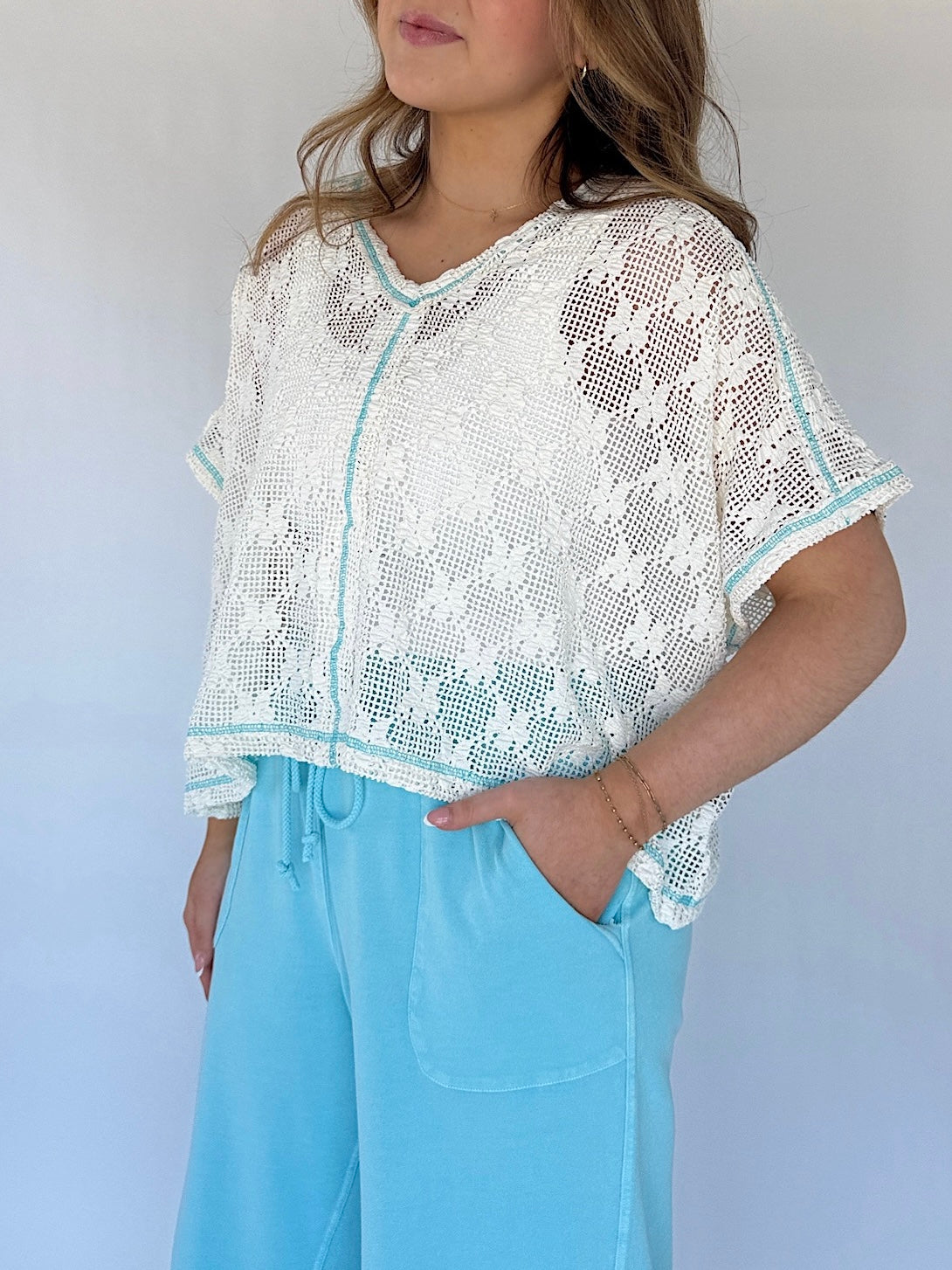 Person wearing a white lace top with blue trim and light blue pants against a plain background