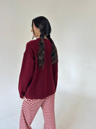 A woman shown from the back wearing a burgundy knit sweater and red-and-white striped pants against a plain light background.