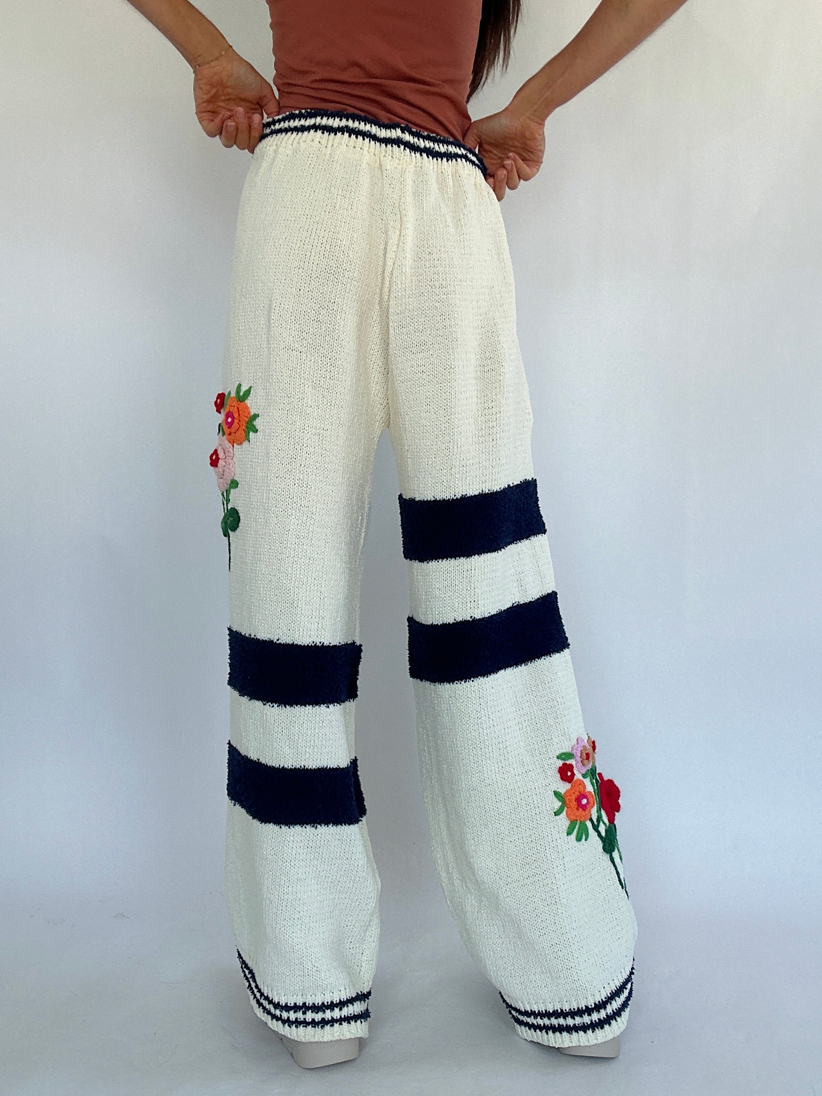 White knitted pants with floral embroidery and navy stripes on a white background showing back