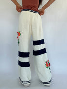White knitted pants with floral embroidery and navy stripes on a white background showing back