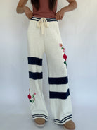 White knitted pants with navy stripes and floral embroidery on a white background
