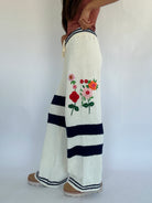 White pants with floral embroidery and navy stripes on a plain background showing side