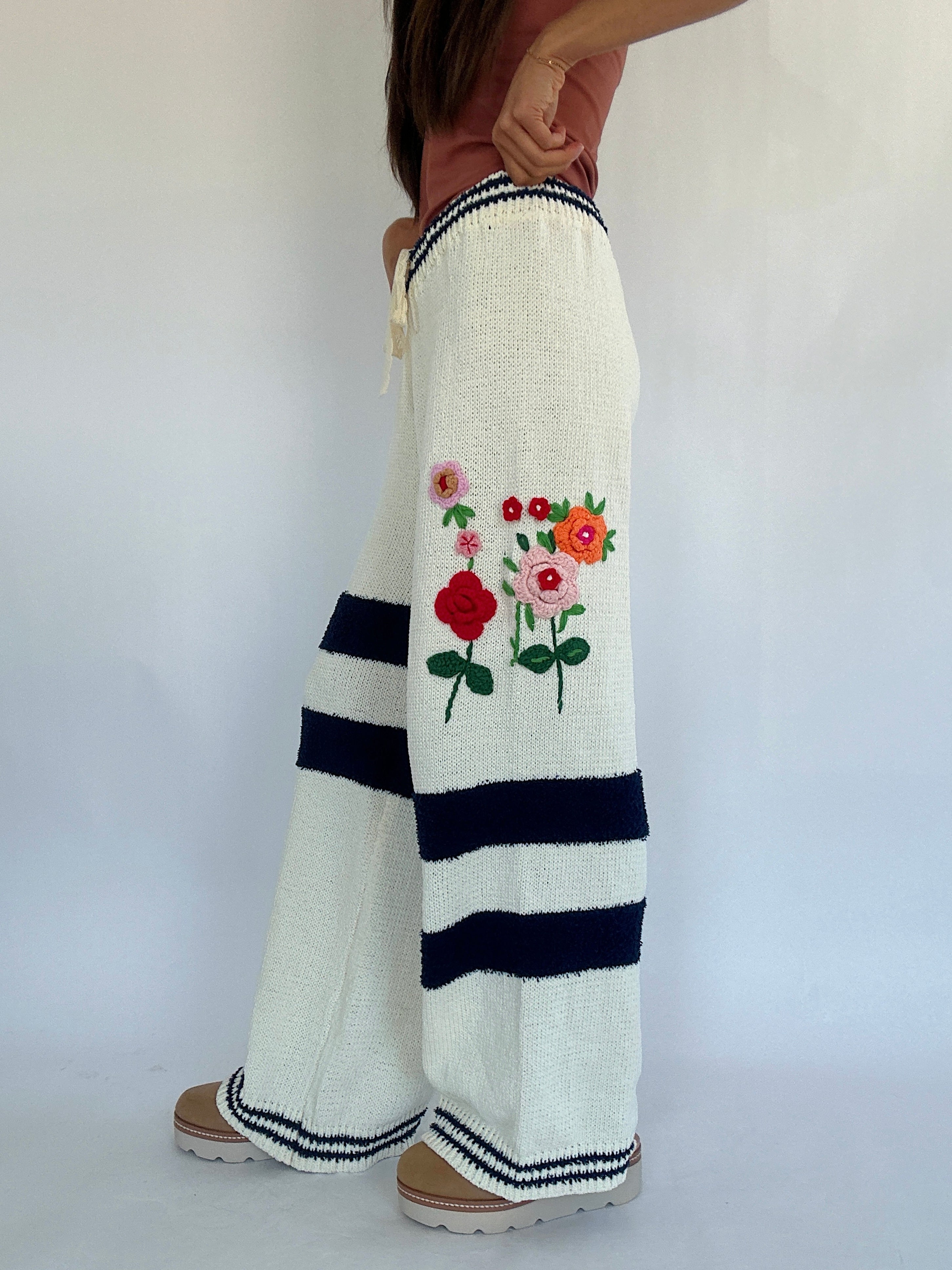 White pants with floral embroidery and navy stripes on a plain background showing side