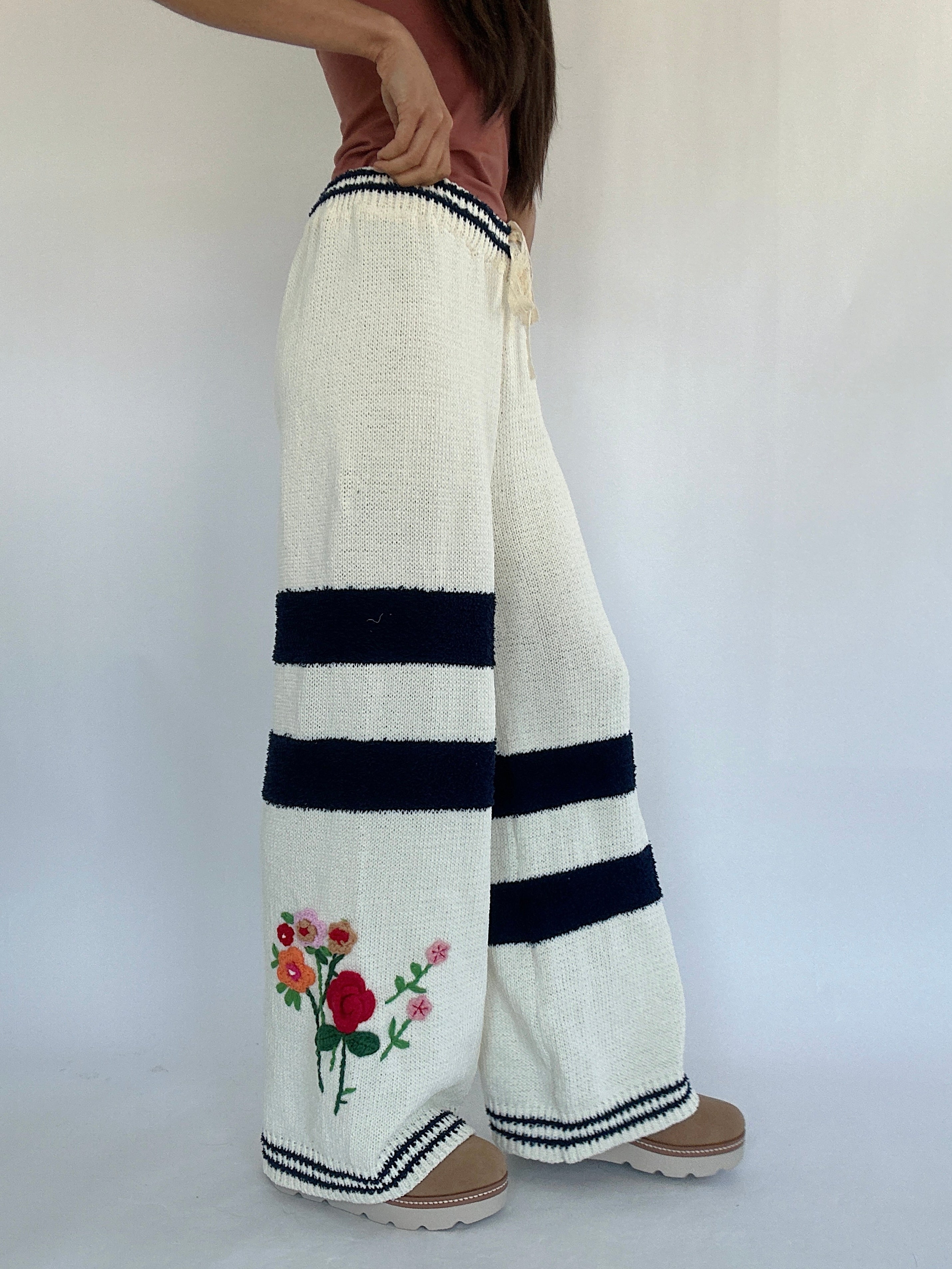 Person wearing white wide-leg pants with black stripes and floral embroidery on a plain background