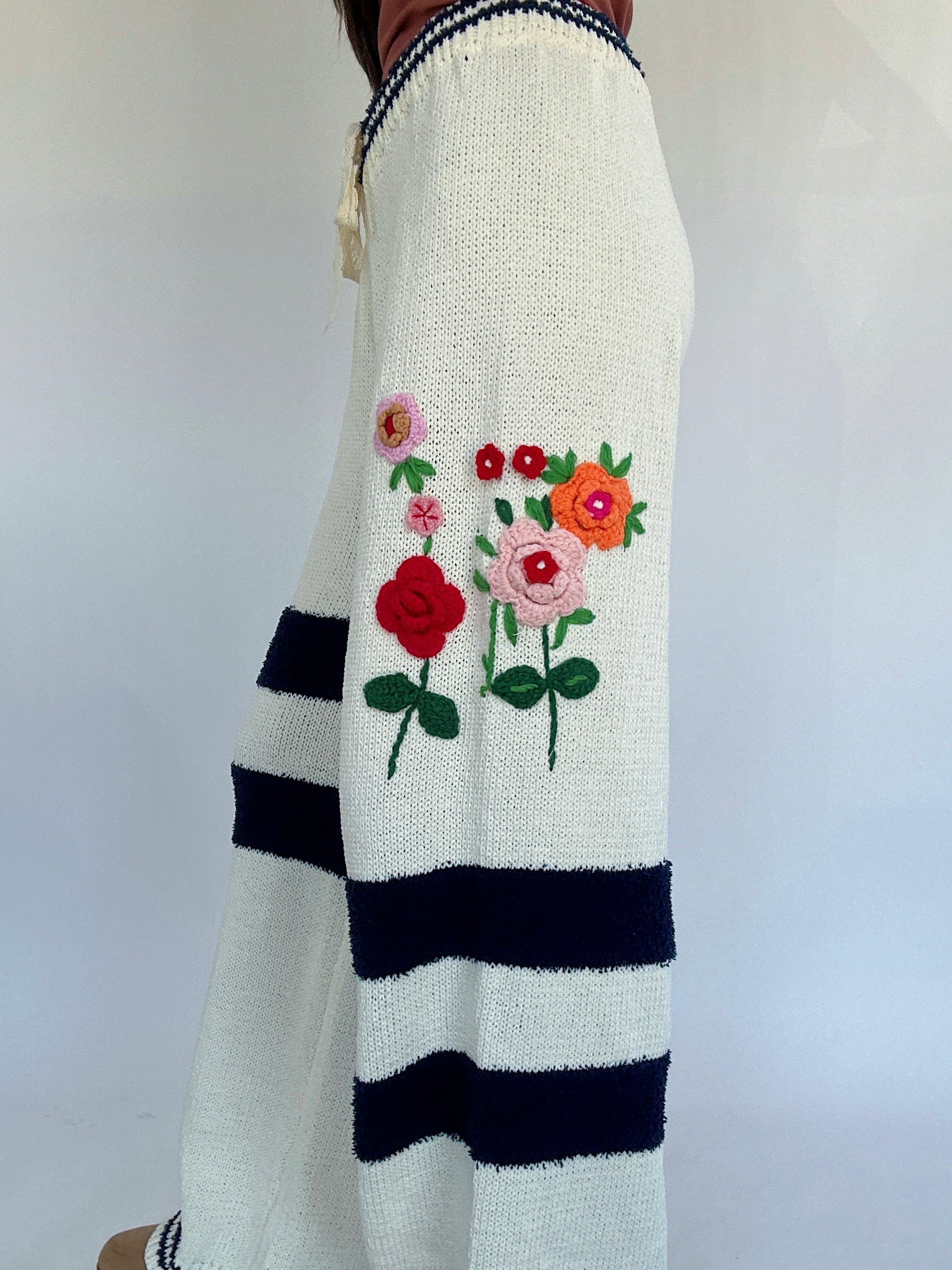 White sweater with 3D floral embroidery and black stripes on a plain background