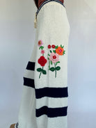 White sweater with 3D floral embroidery and black stripes on a plain background