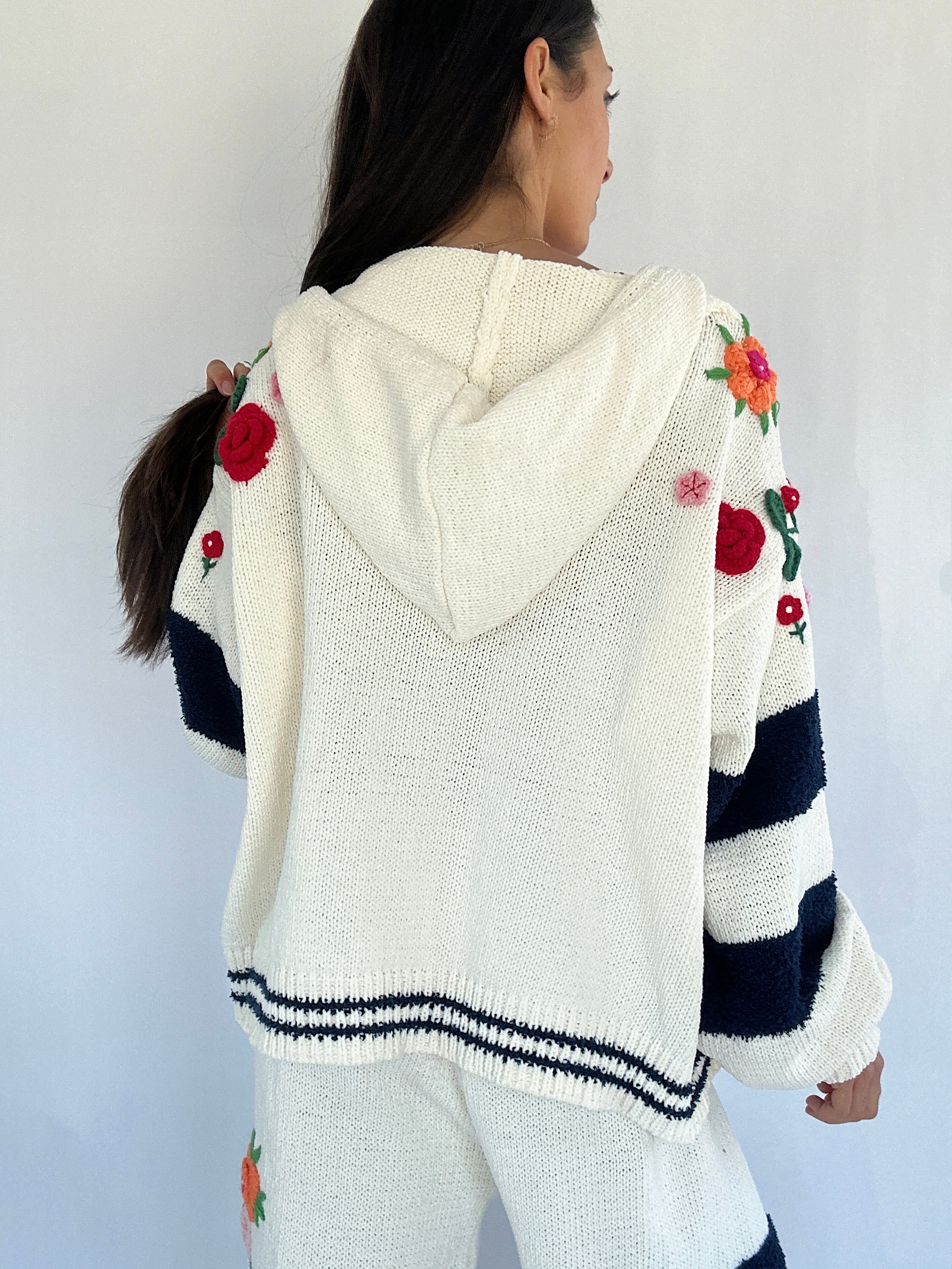 Person wearing a white hoodie with floral embroidery on a plain background back view