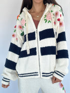 White and navy striped hoodie zip up with floral patterns on a plain background