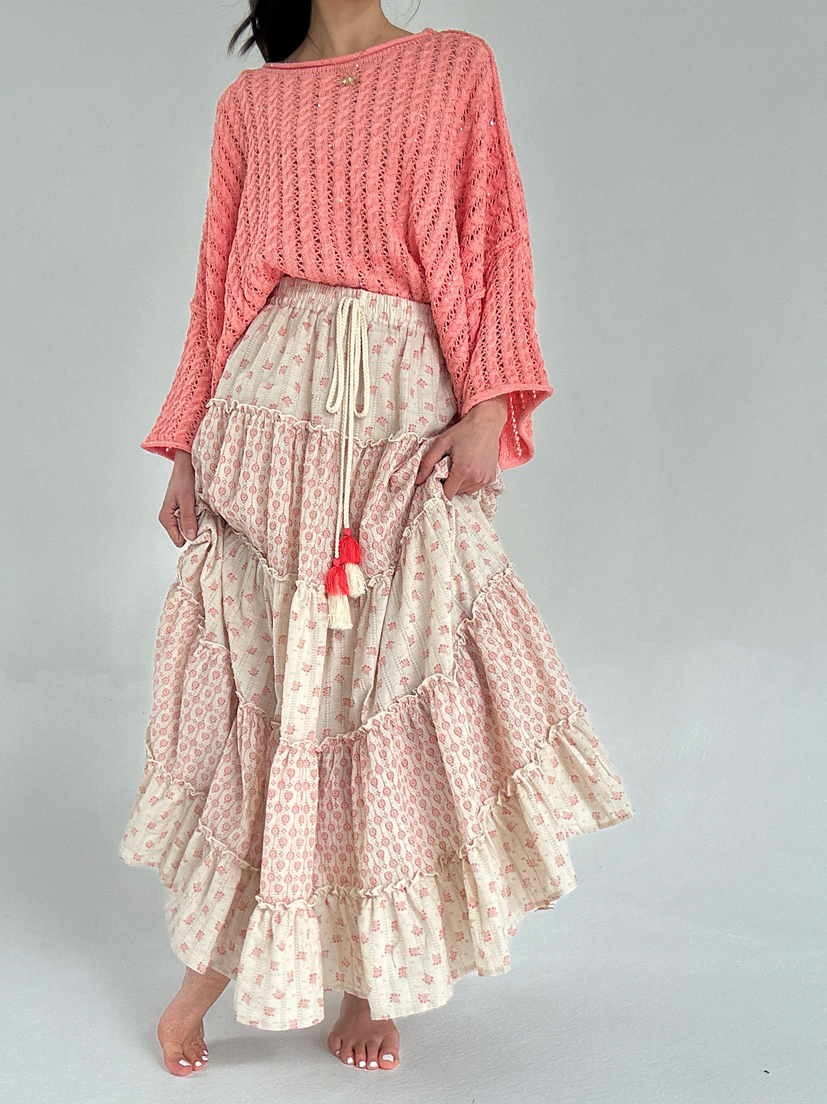 Person wearing a coral knitted top and a long, patterned skirt on a plain background