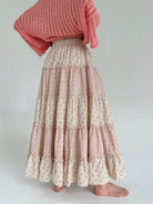 Person wearing a beige and coral patterned skirt and coral top on a white background