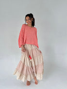 Woman wearing a coral sweater and patterned skirt on a plain background