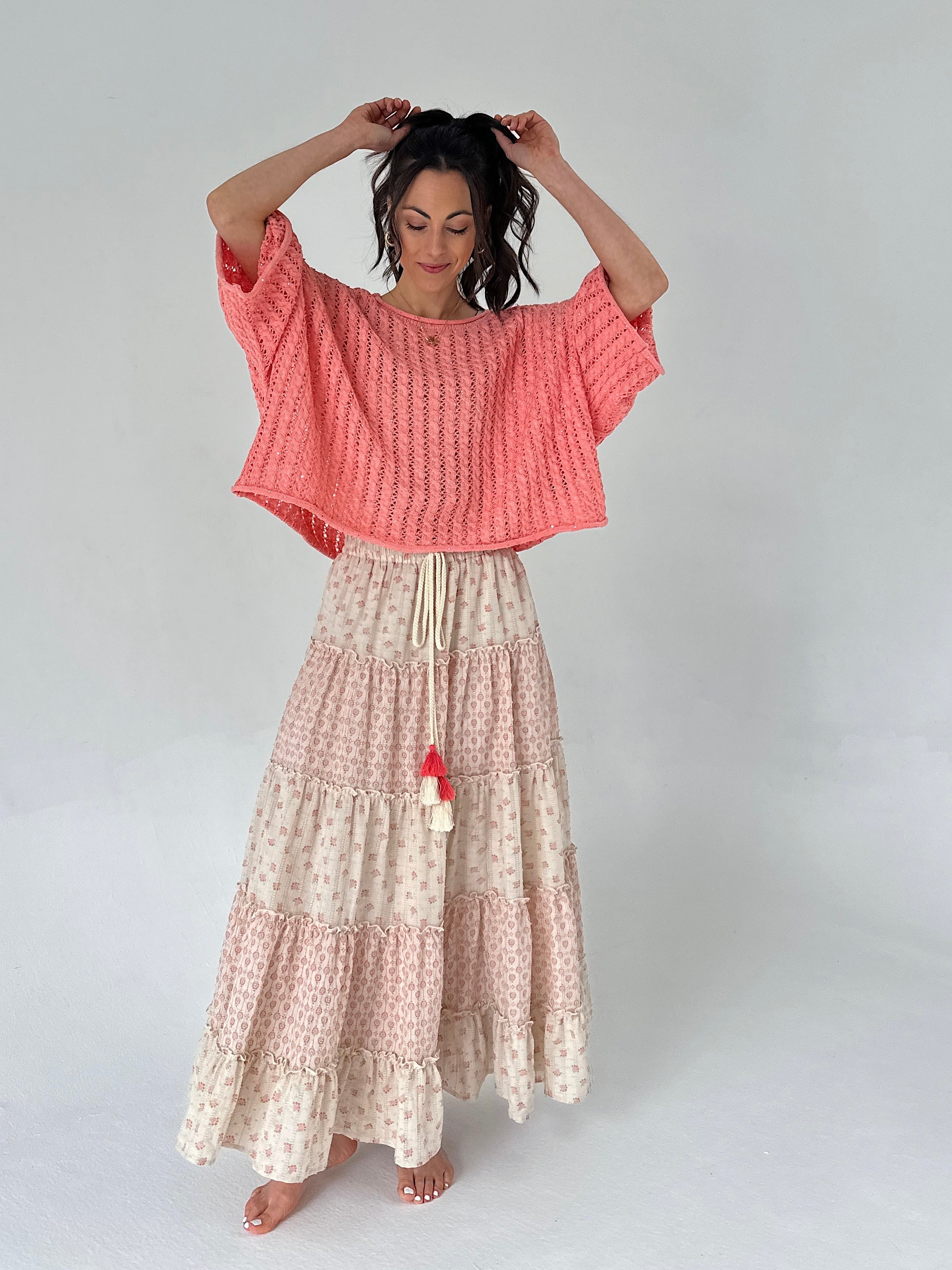 Woman wearing a coral top and patterned skirt on a white background