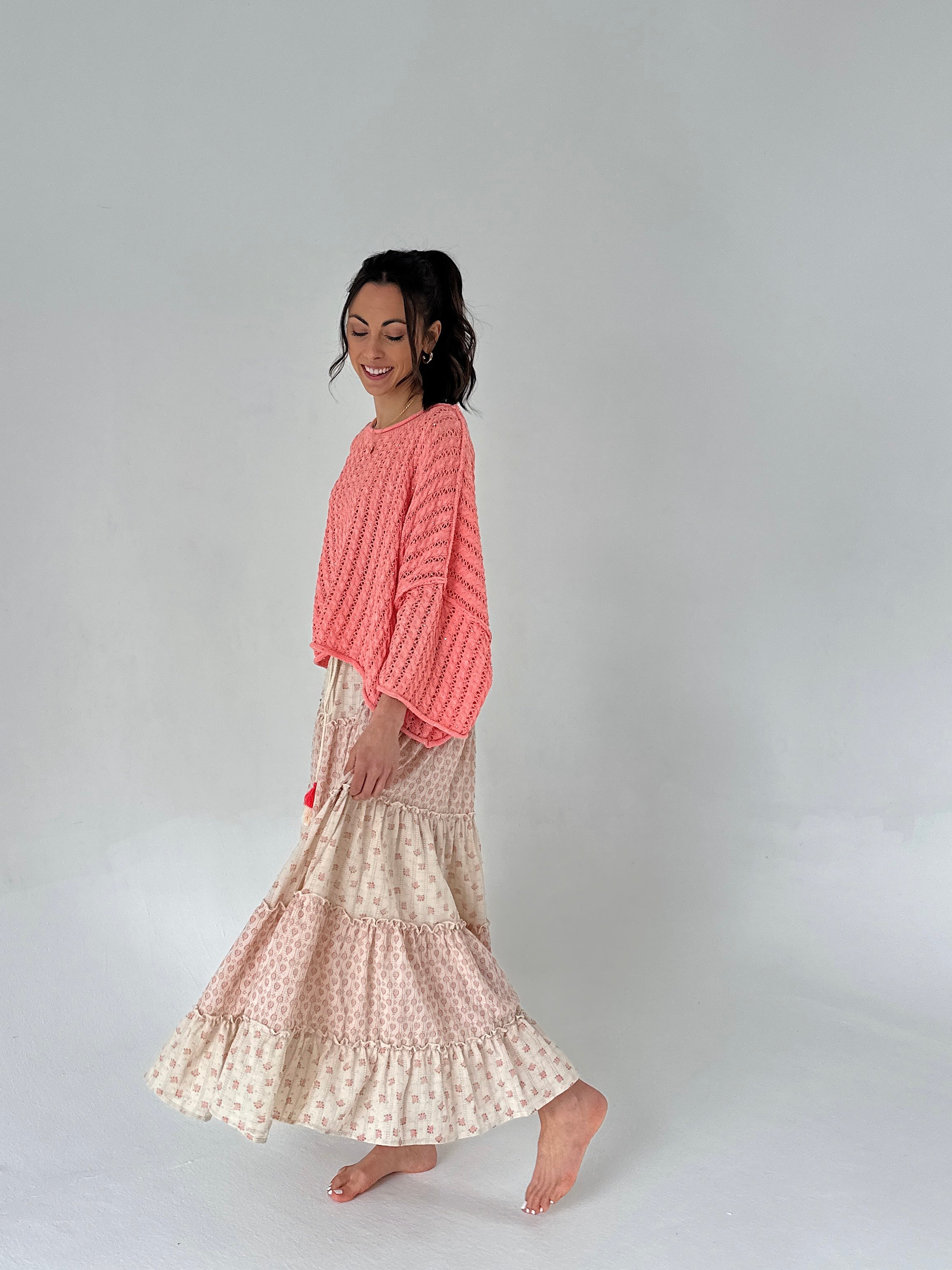 Woman wearing a coral textured top and patterned skirt on a plain background