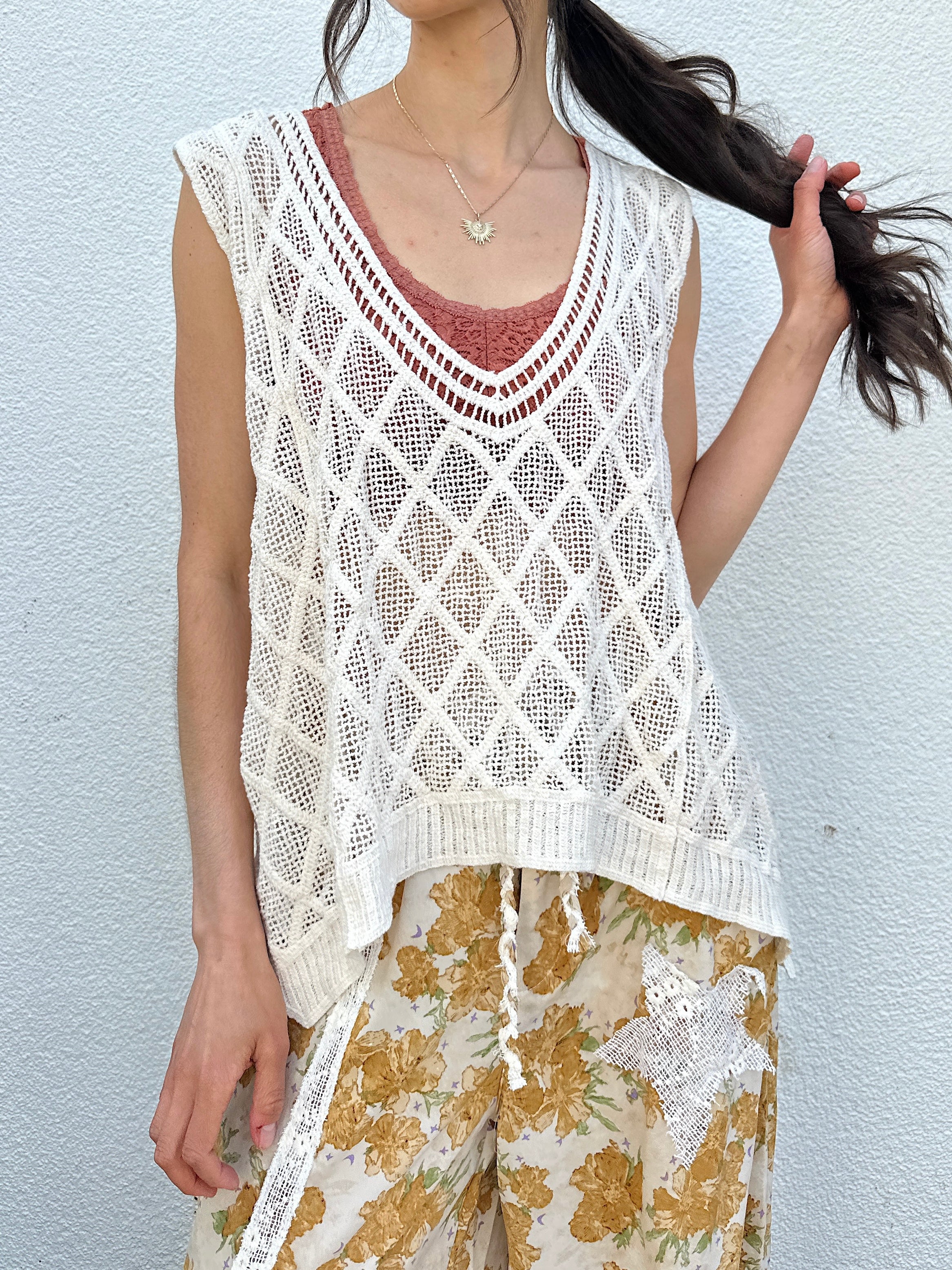 Person wearing a white crochet top with floral yellow pants against a white wall